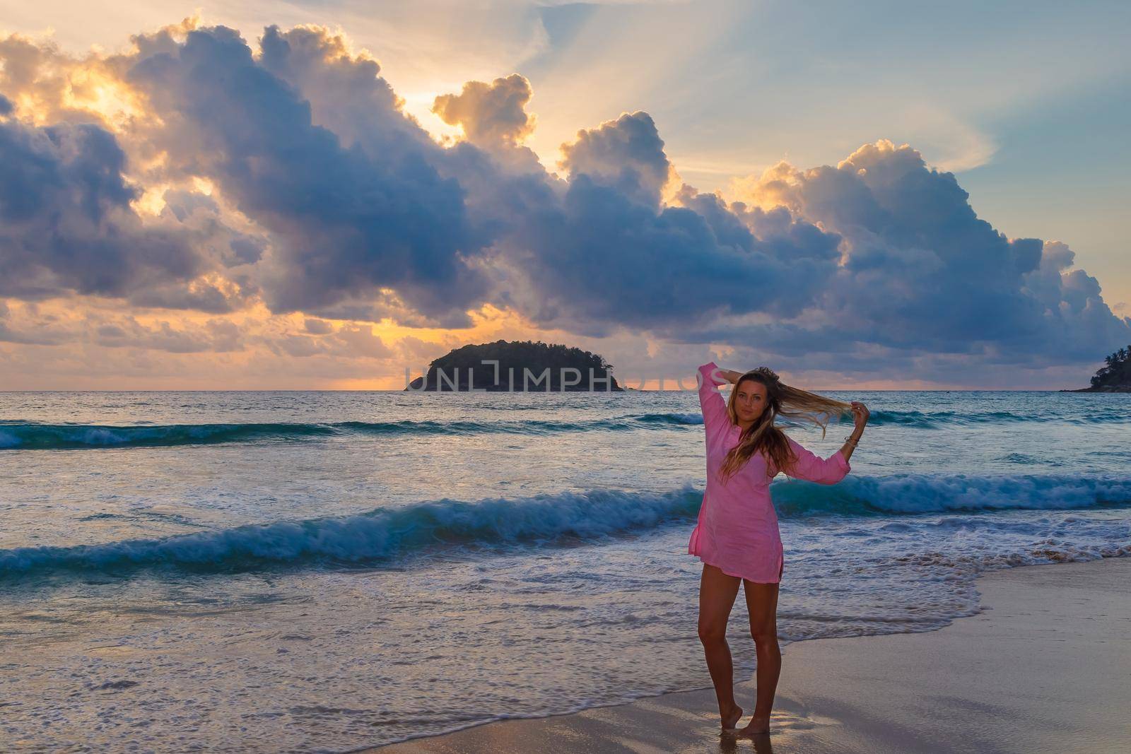 Young beautiful girl in a pink dress by the sea in the rays of the setting sun. Blonde with long hair.