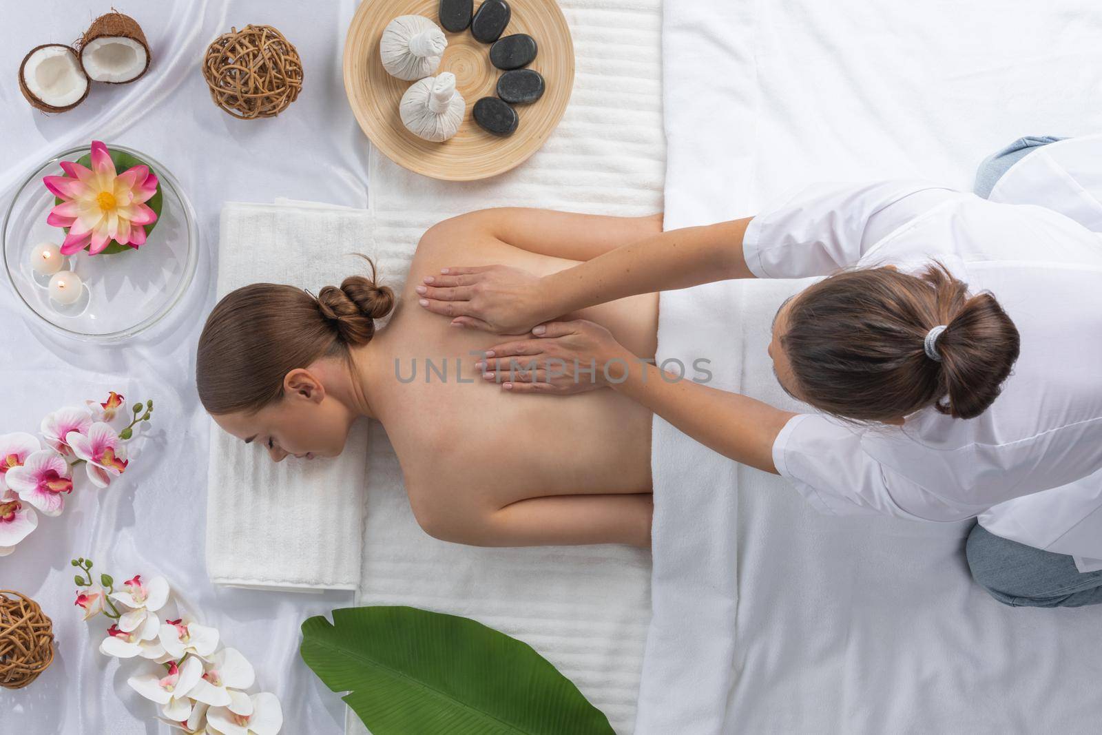 Woman at spa thai massage tow view, beauty treatments concept. Orchid and lotus flowers coconut stones and herb pouches