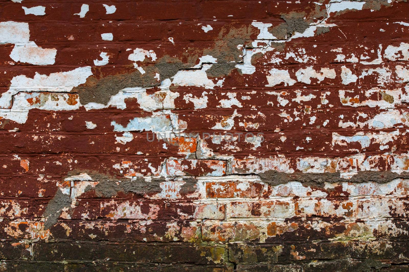 cracked shabby brick wall with old layers of brown and white paint and some mold