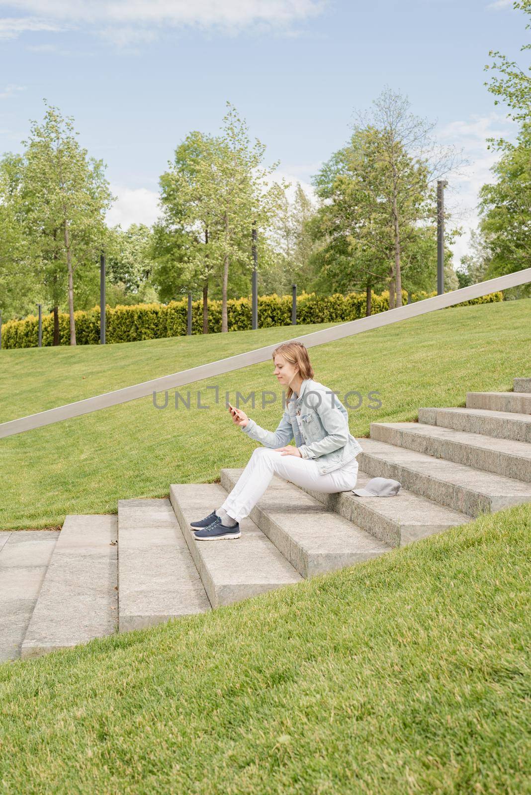 Woman in jeans clothes texting on her mobile phone, sitting on the stairs in the park