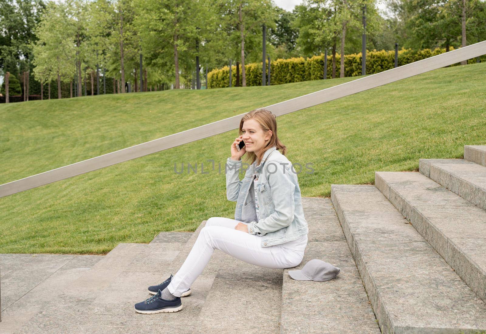 Woman in jeans clothes texting on her mobile phone, sitting on the stairs in the park