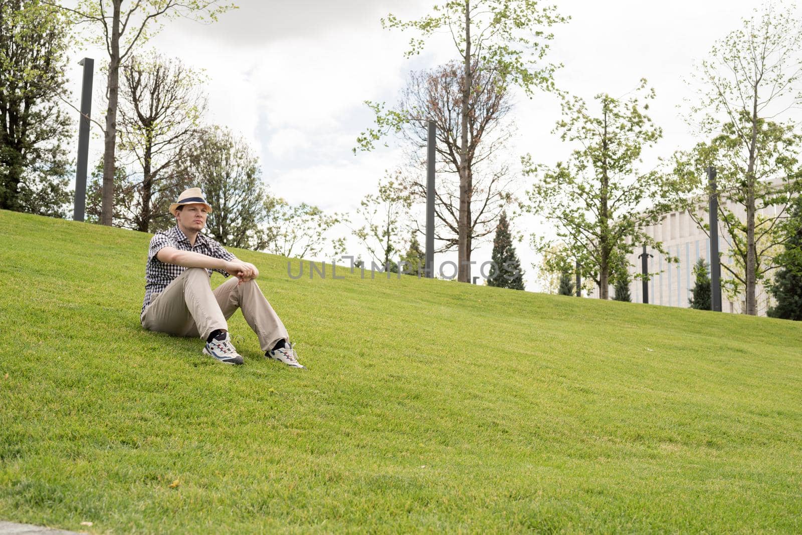 Young thoughtful man sitting on the grass in the park by Desperada