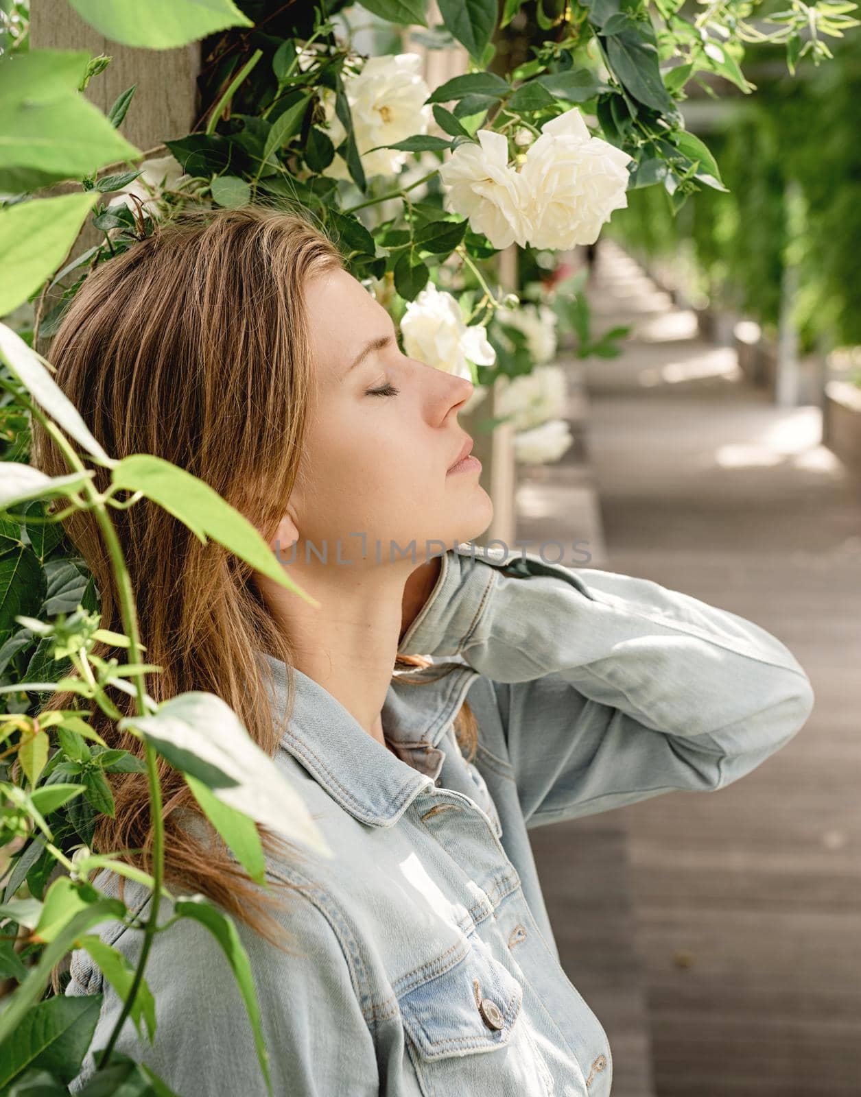 Beautiful young blond woman standing in white roses in a garden or park , eyes closed