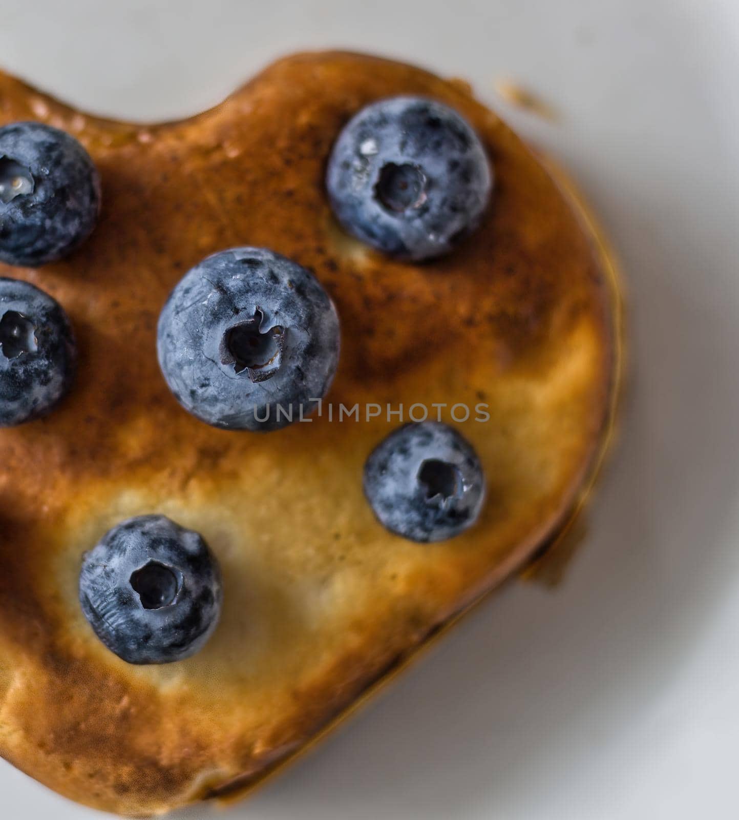 Healthy food concept displaying vertical image of half heart shape pan cake with blueberries fruit on top isolated on white background