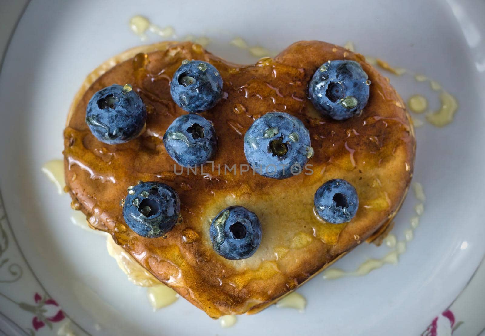 Healthy food concept displaying image of full heart shape pan cake with blueberries fruit and honey on top isolated on white background