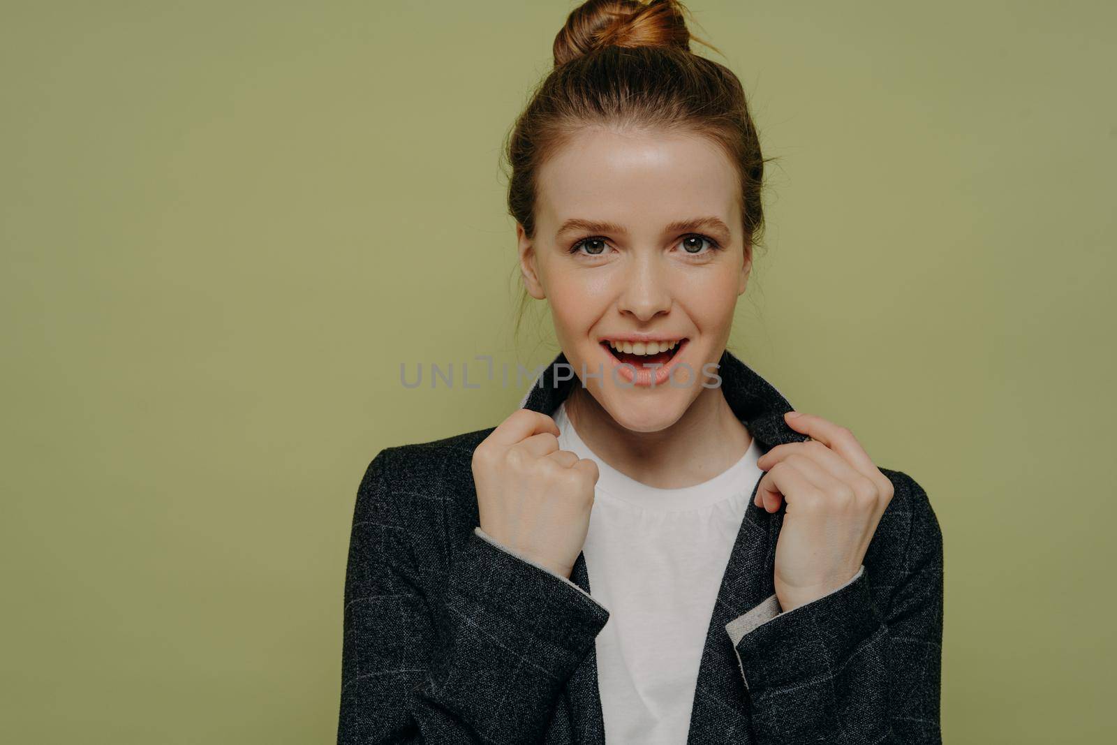 Headshot portrait of young overjoyed trendy woman in casual clothes holding collar of jacket and looking at camera with excited face expression, positive female posing in studio over green background