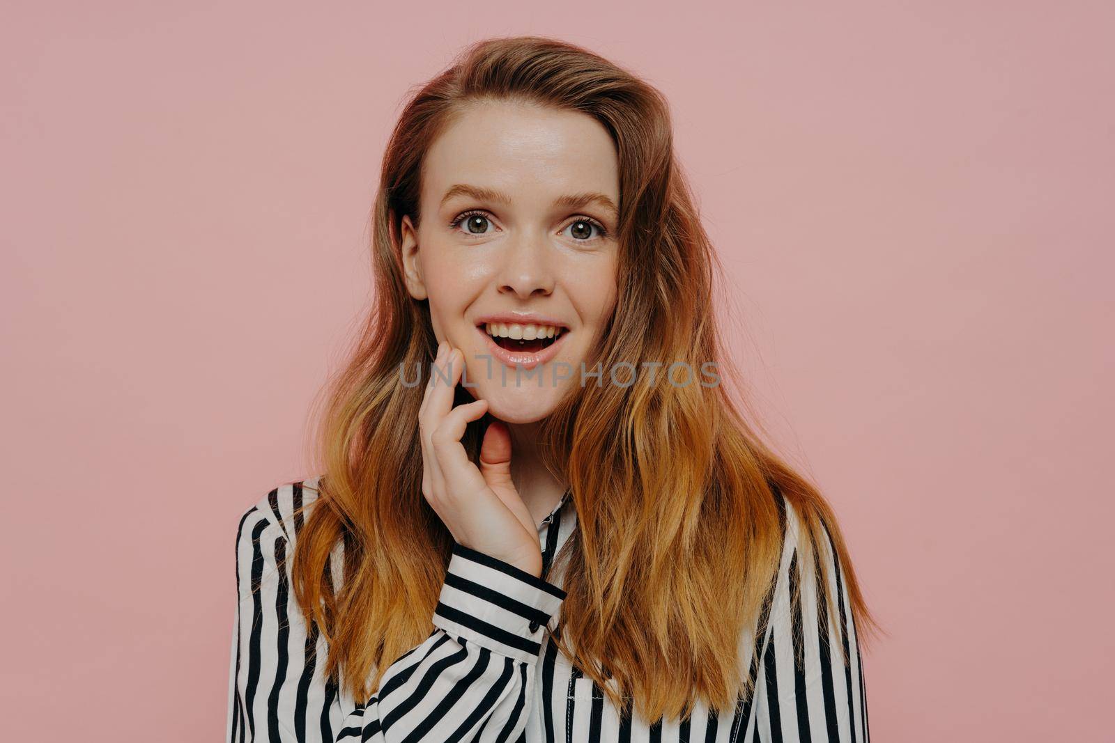 Happy young teenage girl demonstrating wow expression while posing over pink background by vkstock