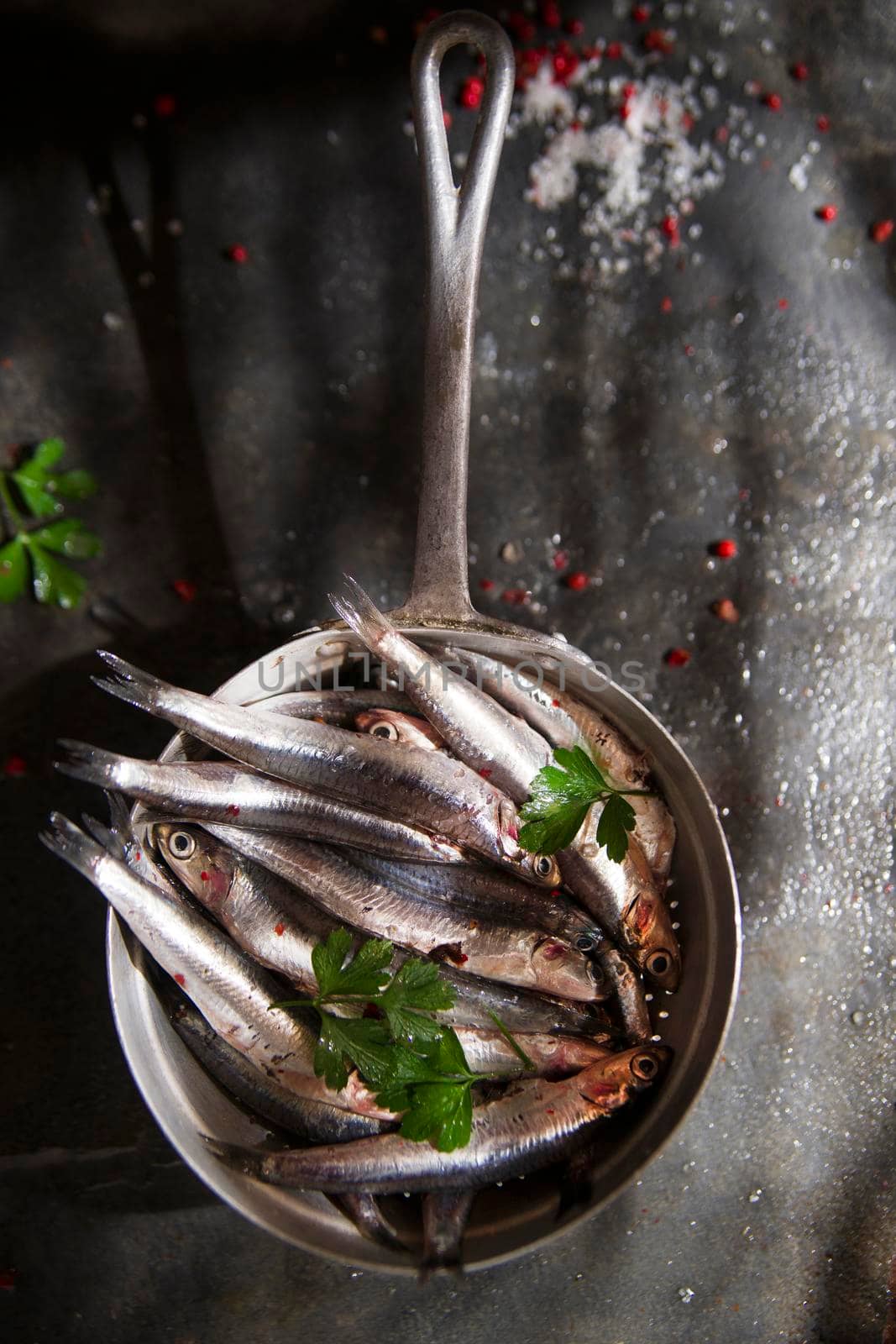 Presentation of a small strainer raw anchovies on a black background