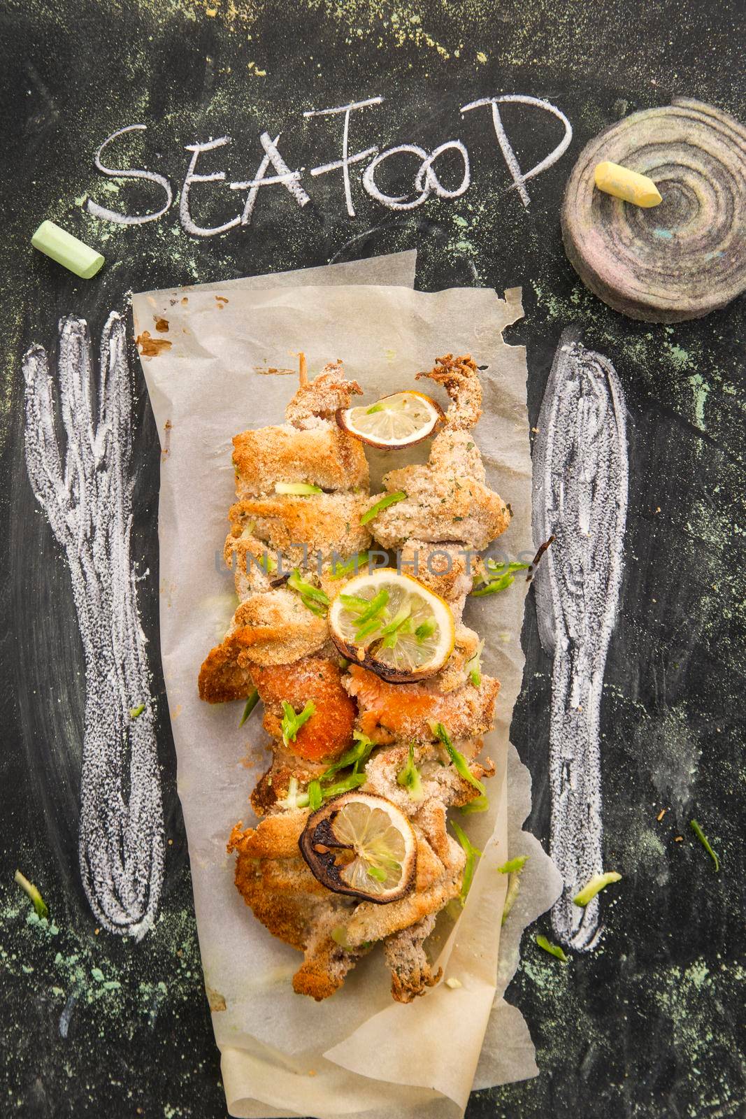 Presentation of fish skewer au gratin on chalkboard background