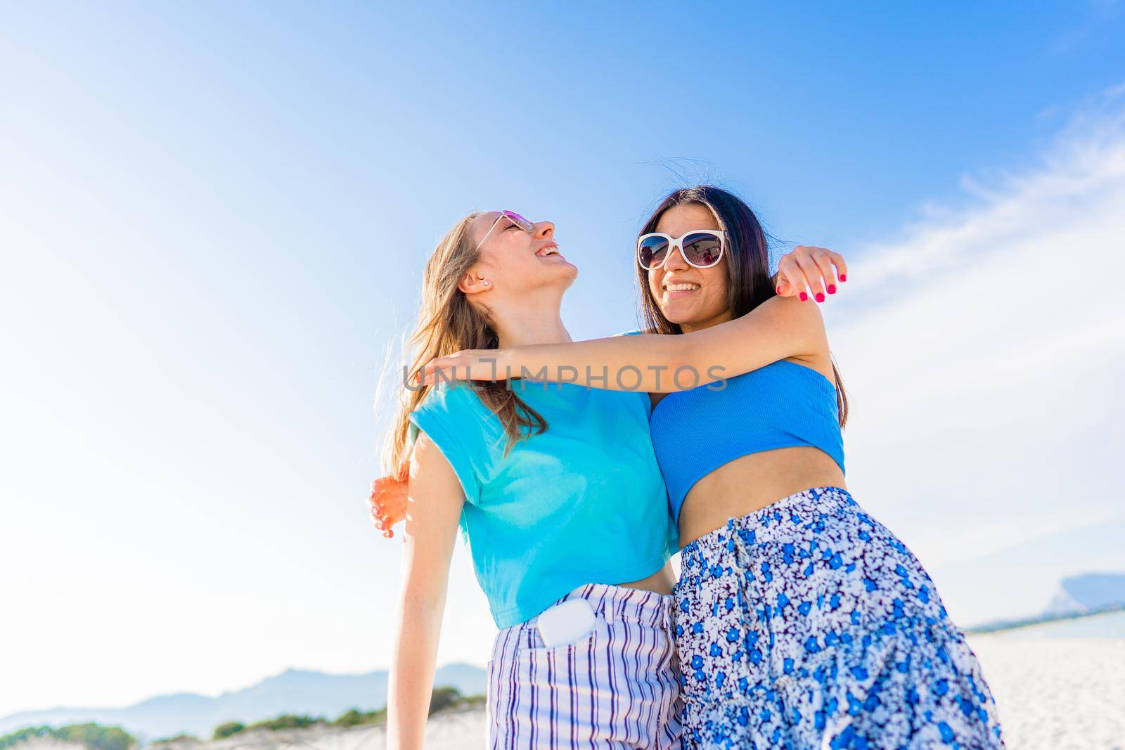 Bottom view of girls couple embracing laughing enjoying life on vacations at sea ocean tropical resort. Glamour photography of two 20s young women hugging on beach in summer travel. Happiness concept