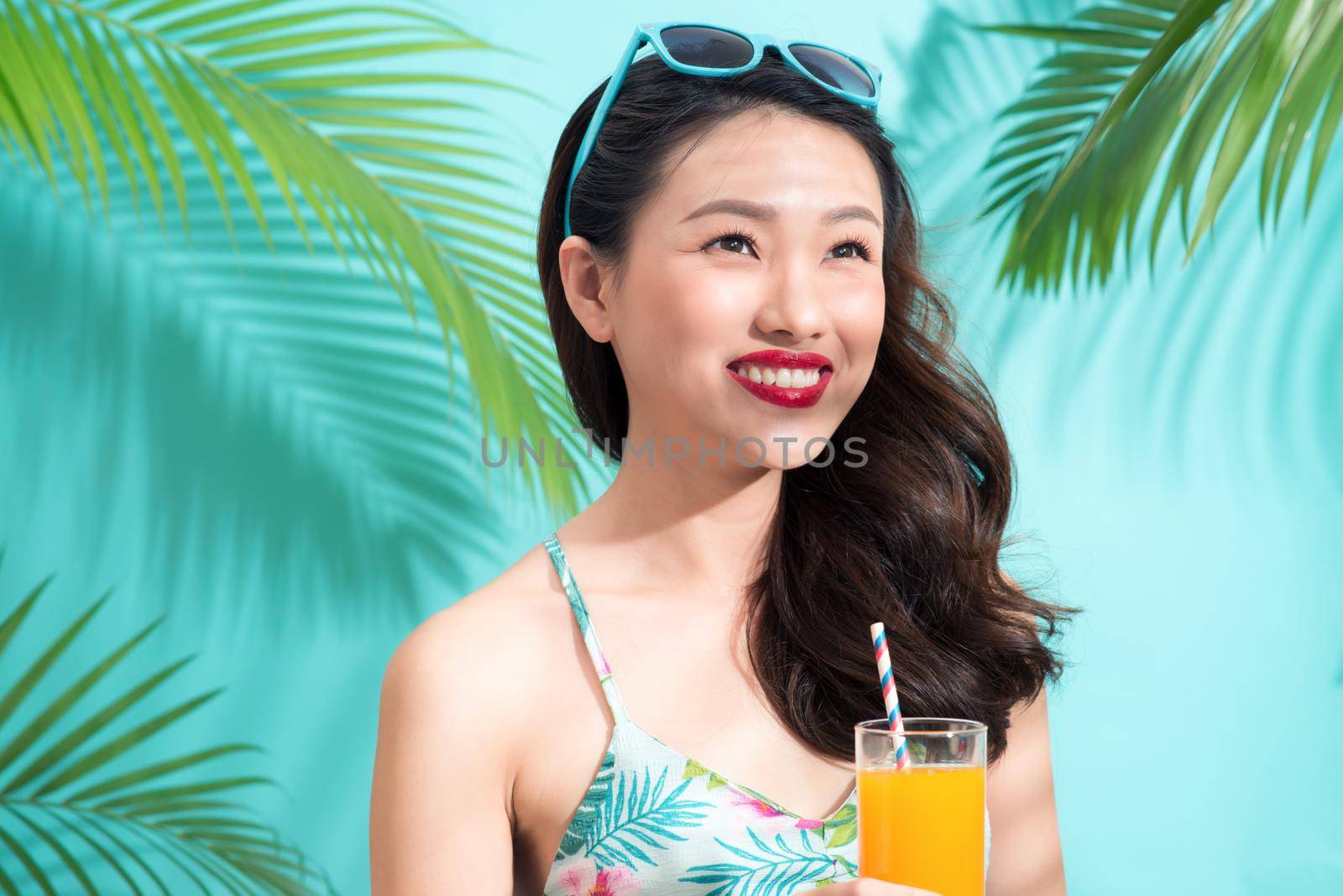 Young asian woman drinks  juice from glass over colorful blue background by makidotvn