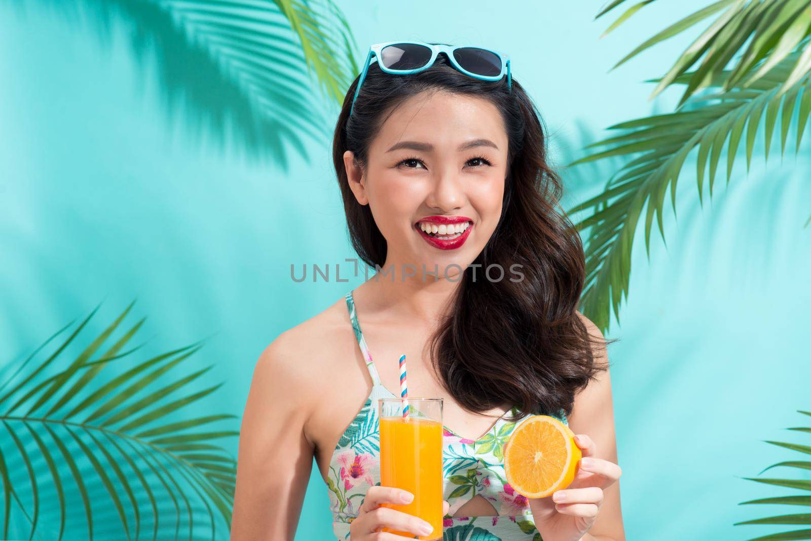 Young asian woman drinks  juice from glass over colorful blue background