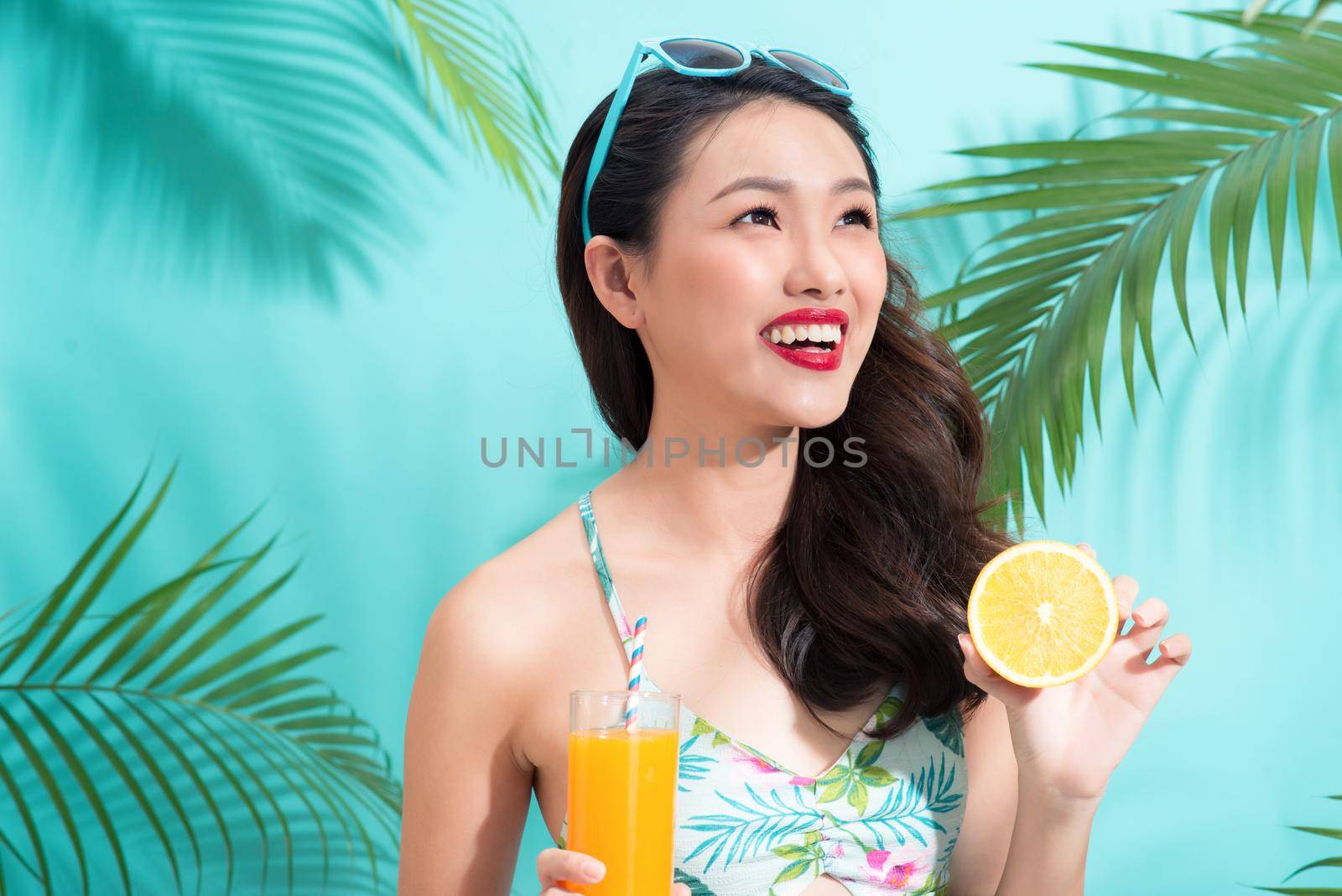 Fashion pretty woman drinks  juice from glass over colorful blue background by makidotvn