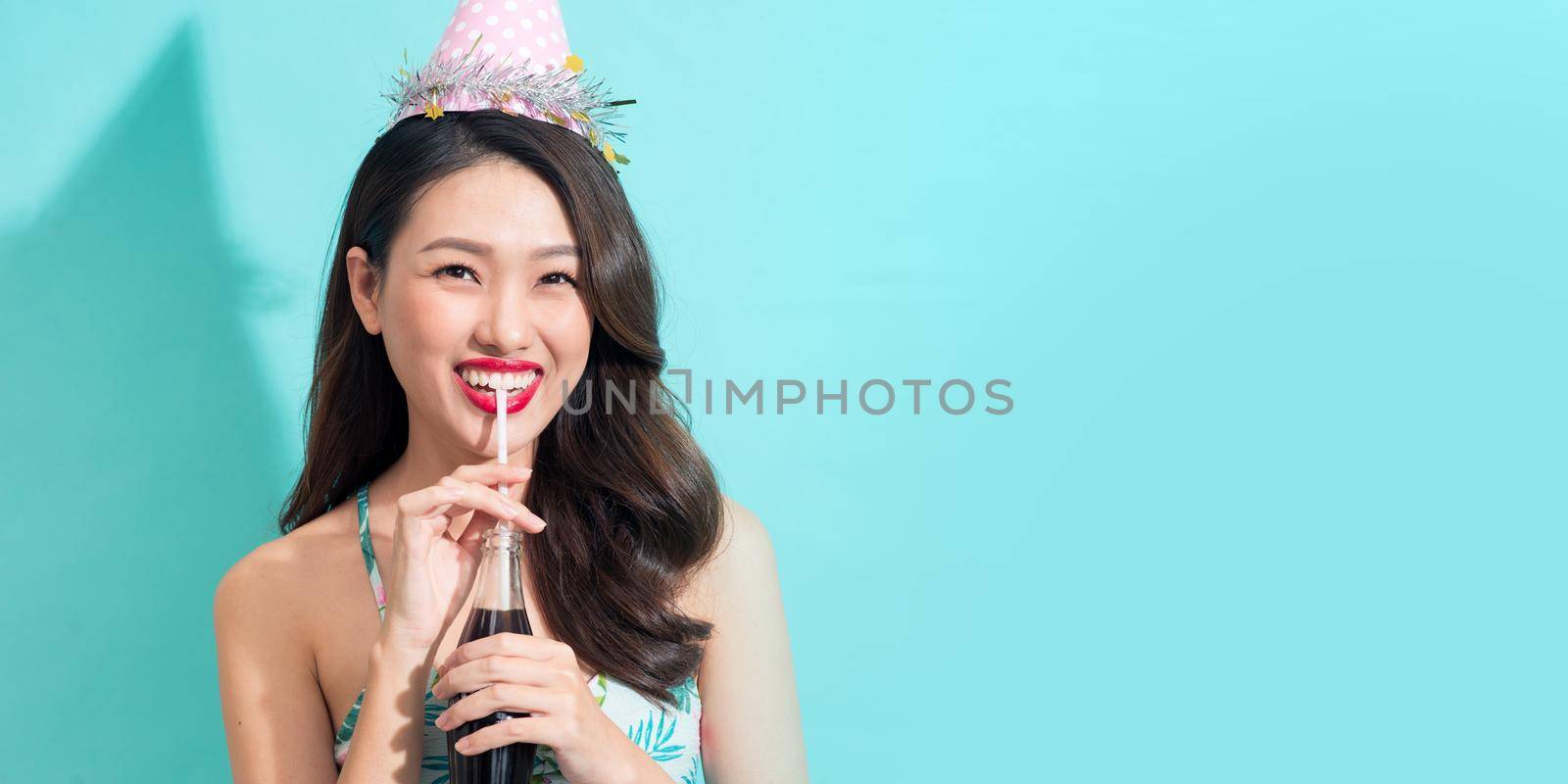 Banner size. Fashion pretty woman drinks coke from bottle over colorful blue background by makidotvn