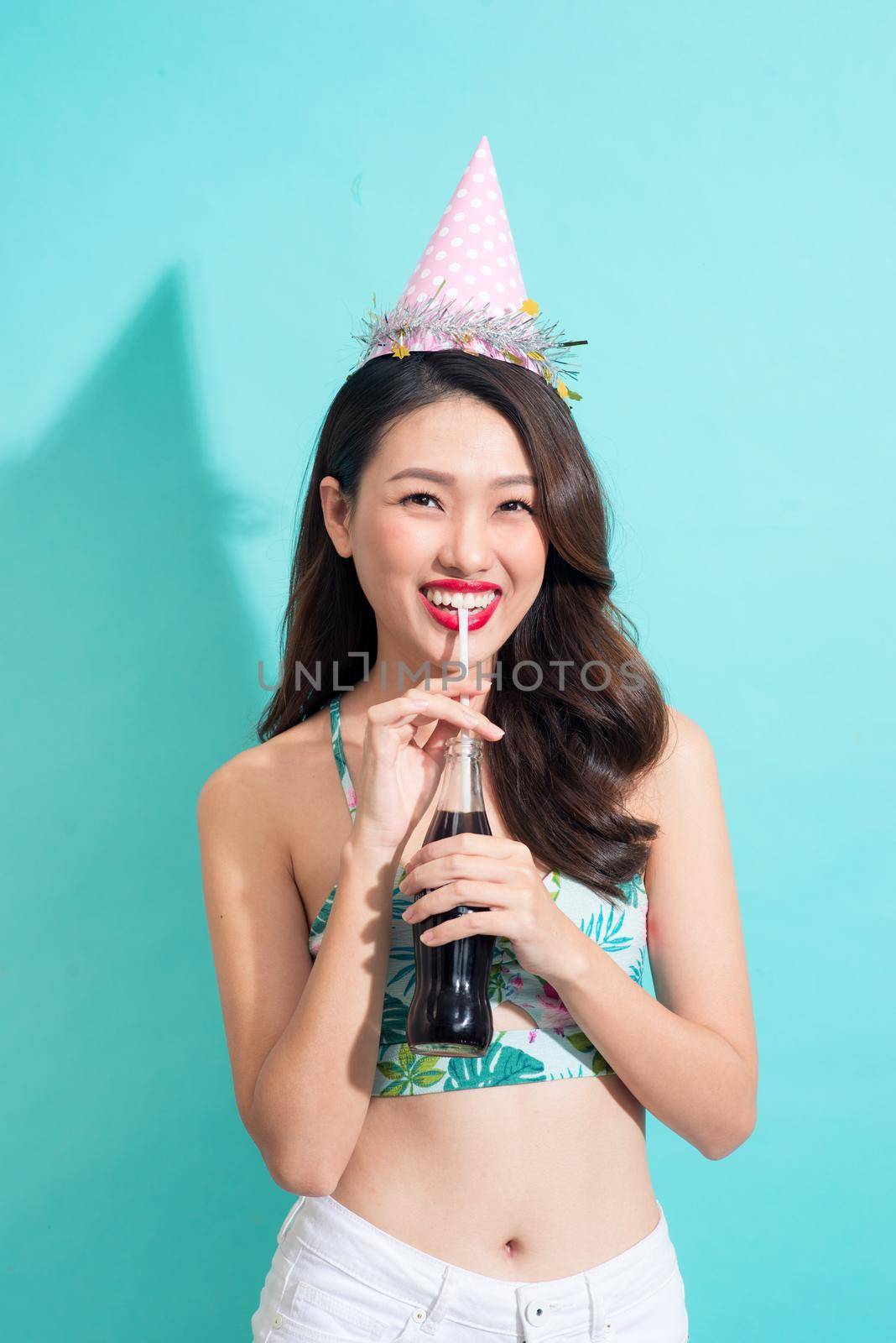 Fashion pretty woman drinks coke from bottle over colorful blue background