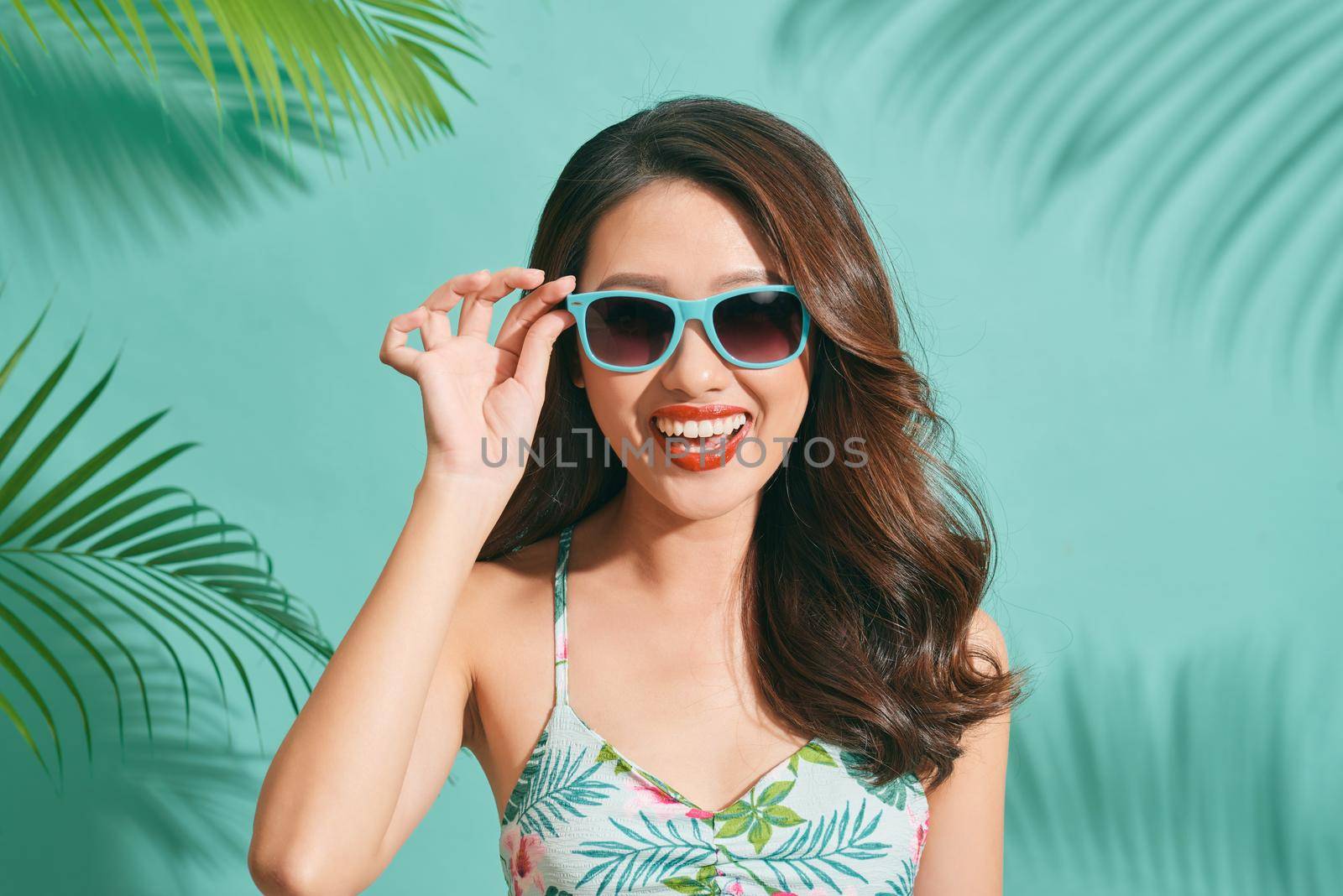 Asian young woman wearing a bikini and sunglasses having fun on blue background by makidotvn