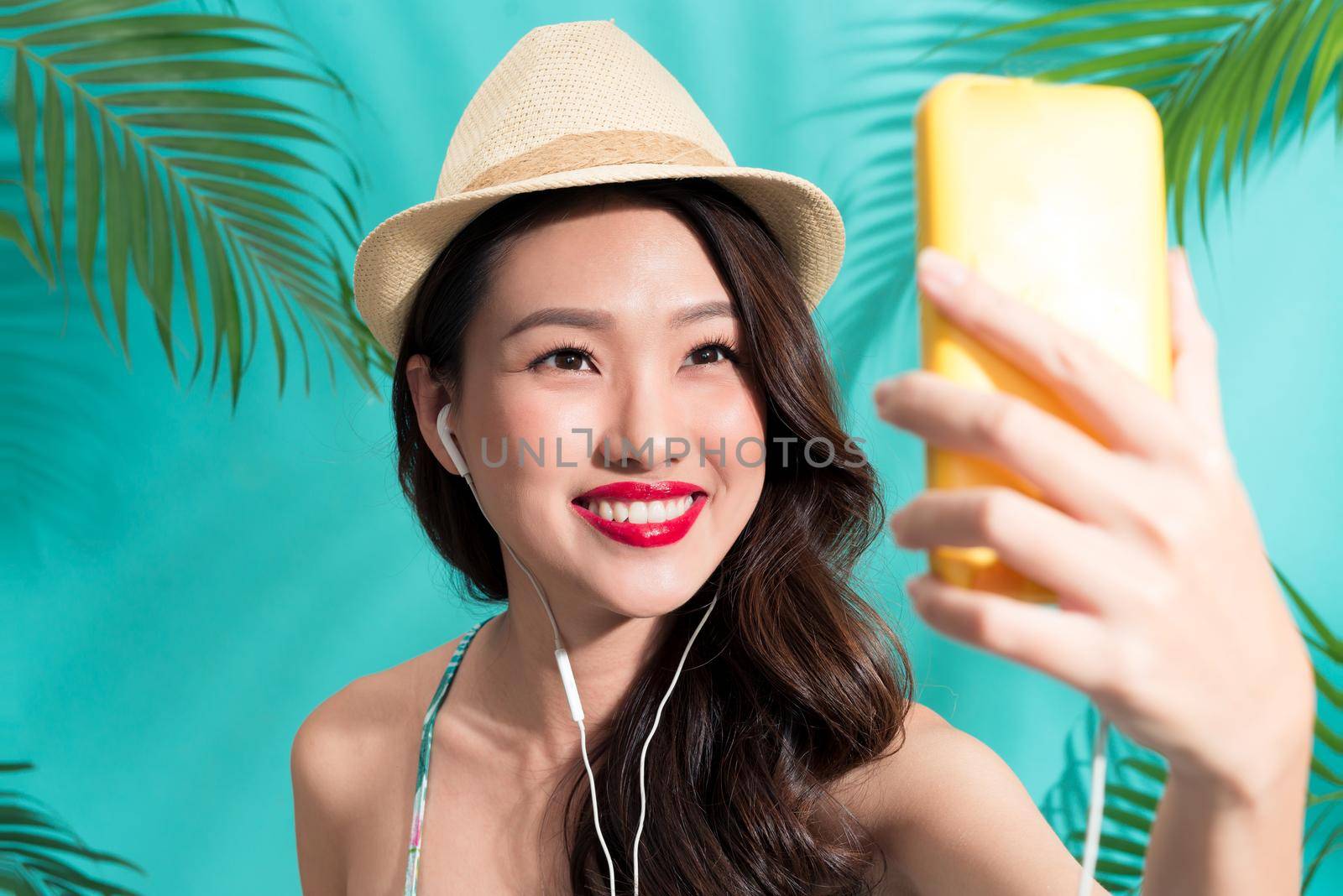 Fashion pretty woman with hat standing and taking selfie photo over colorful blue background