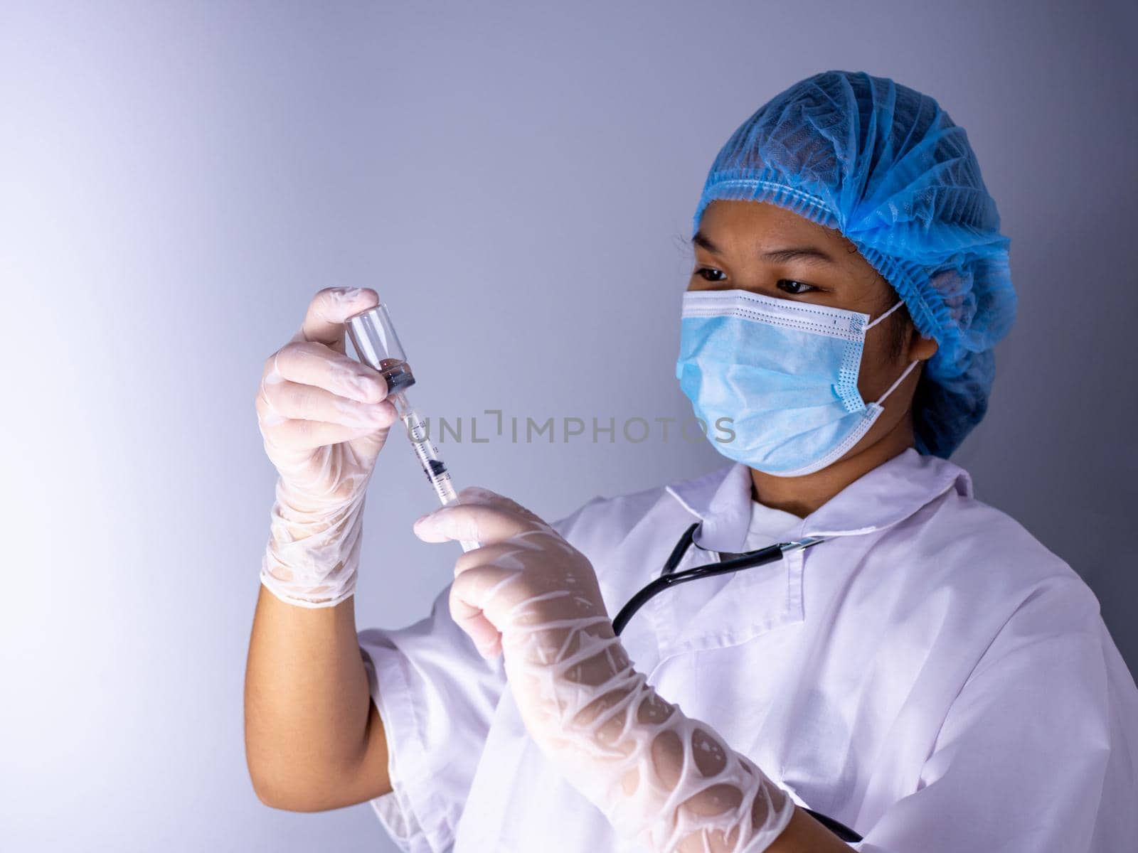 Studio portrait of a female doctor wearing a mask and wearing a hat. In hand was a bottle of vaccine and a sling of syringes. standing on a white background. Studio shot background, COVID-19 concept by Unimages2527