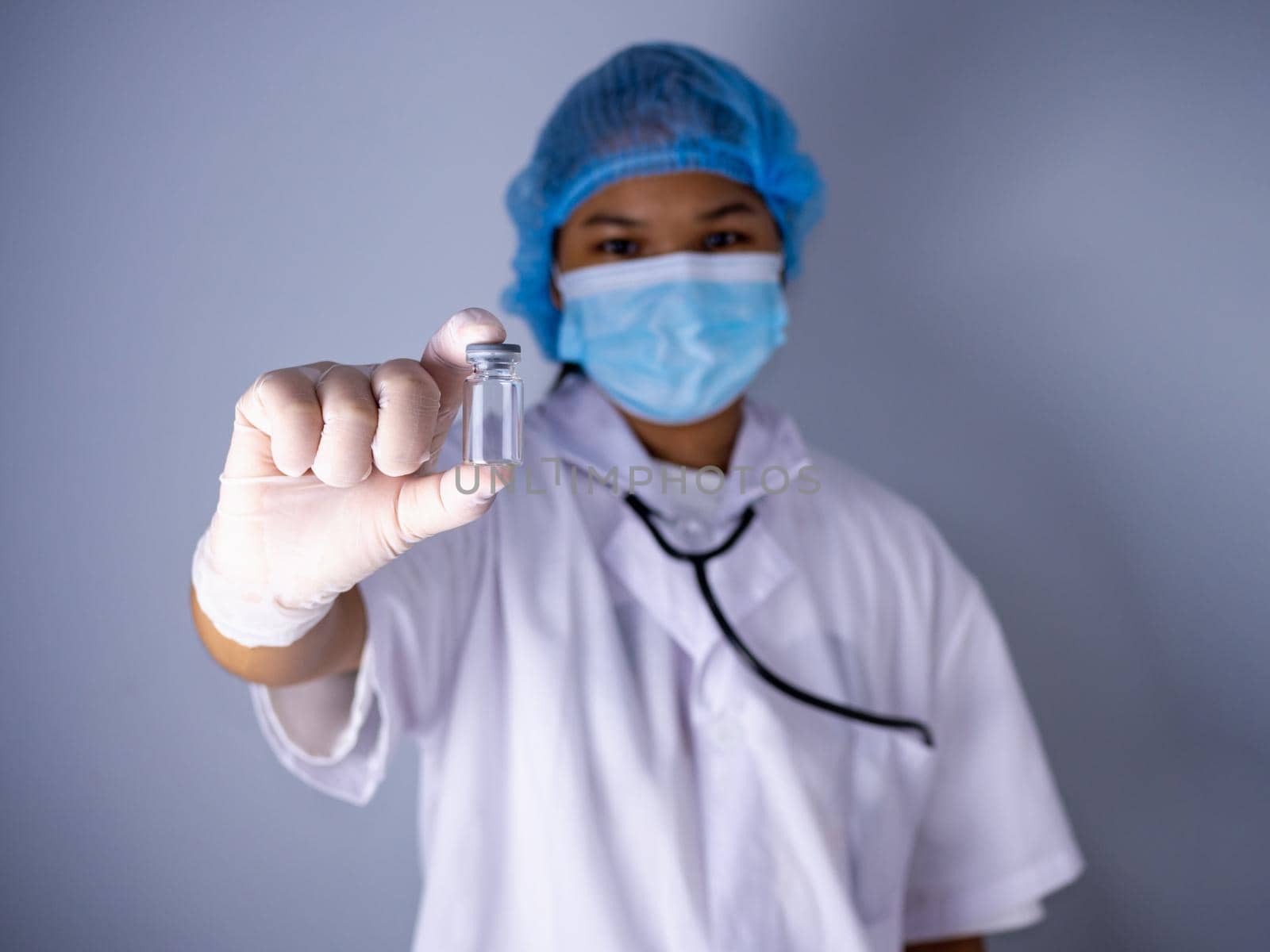 Studio portrait of a female doctor wearing a mask and wearing a hat. in the hand of the vaccine bottle and stretched out his arms in front standing on a white background. studio shot background, COVID-19 concept by Unimages2527