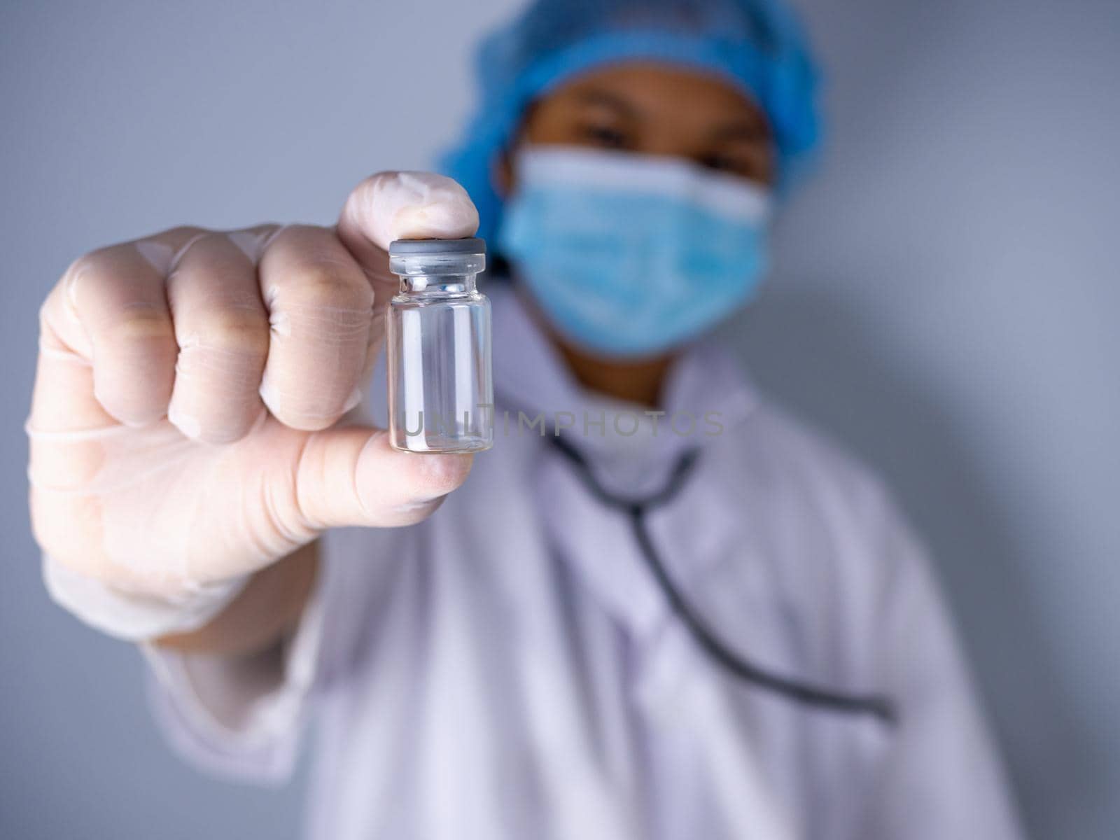 Studio portrait of a female doctor wearing a mask and wearing a hat. in the hand of the vaccine bottle and stretched out his arms in front standing on a white background. studio shot background, COVID-19 concept by Unimages2527