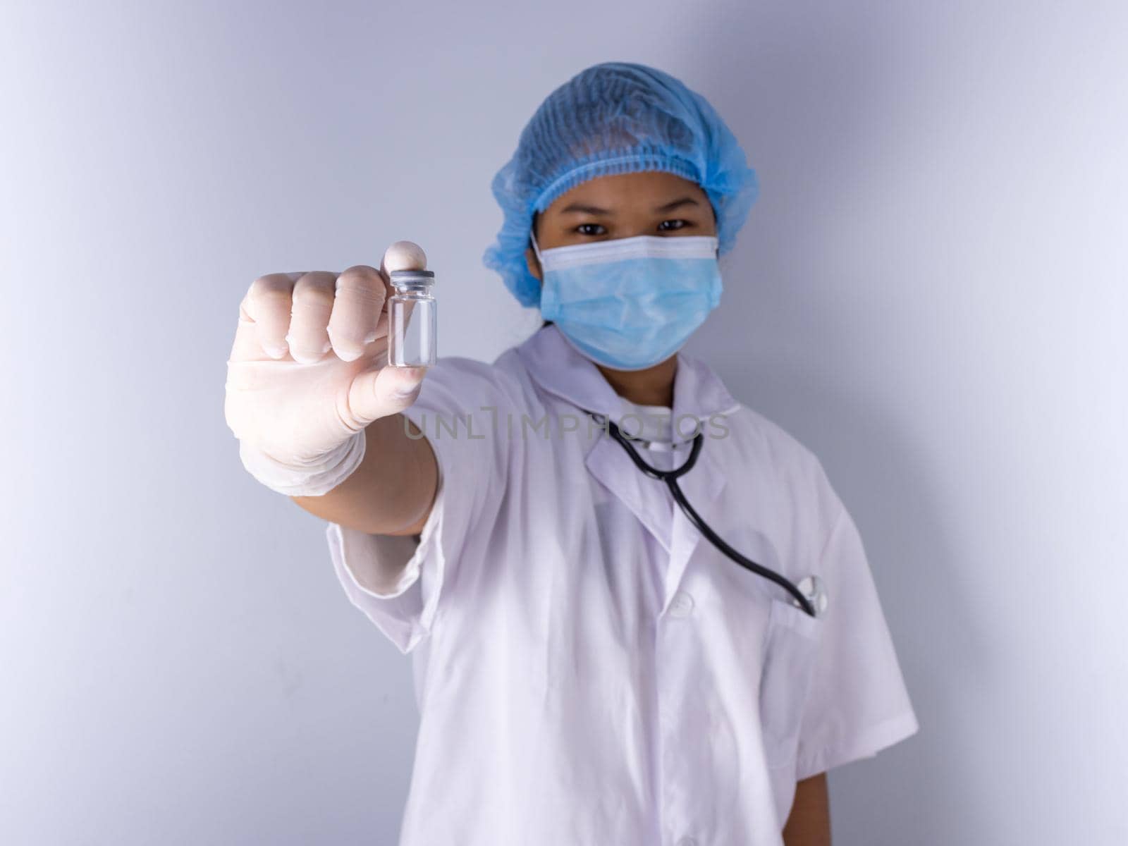Studio portrait of a female doctor wearing a mask and wearing a hat. in the hand of the vaccine bottle and stretched out his arms in front standing on a white background. studio shot background, COVID-19 concept by Unimages2527