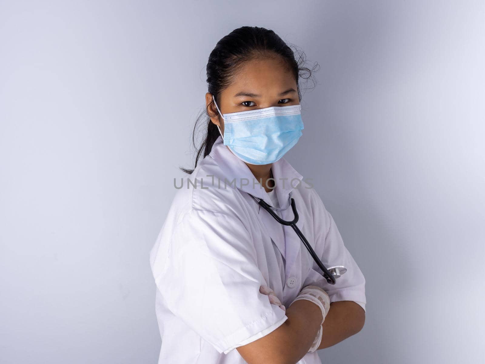 Studio portrait of a female doctor wearing a mask standing on a white background There was a slight light on his face. by Unimages2527