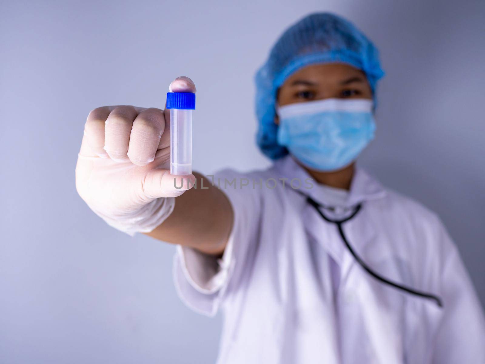 Portrait of a female doctor wearing a mask and wearing a hat Stand holding an empty vaccine or pill bottle.Medical concept and treatment. by Unimages2527