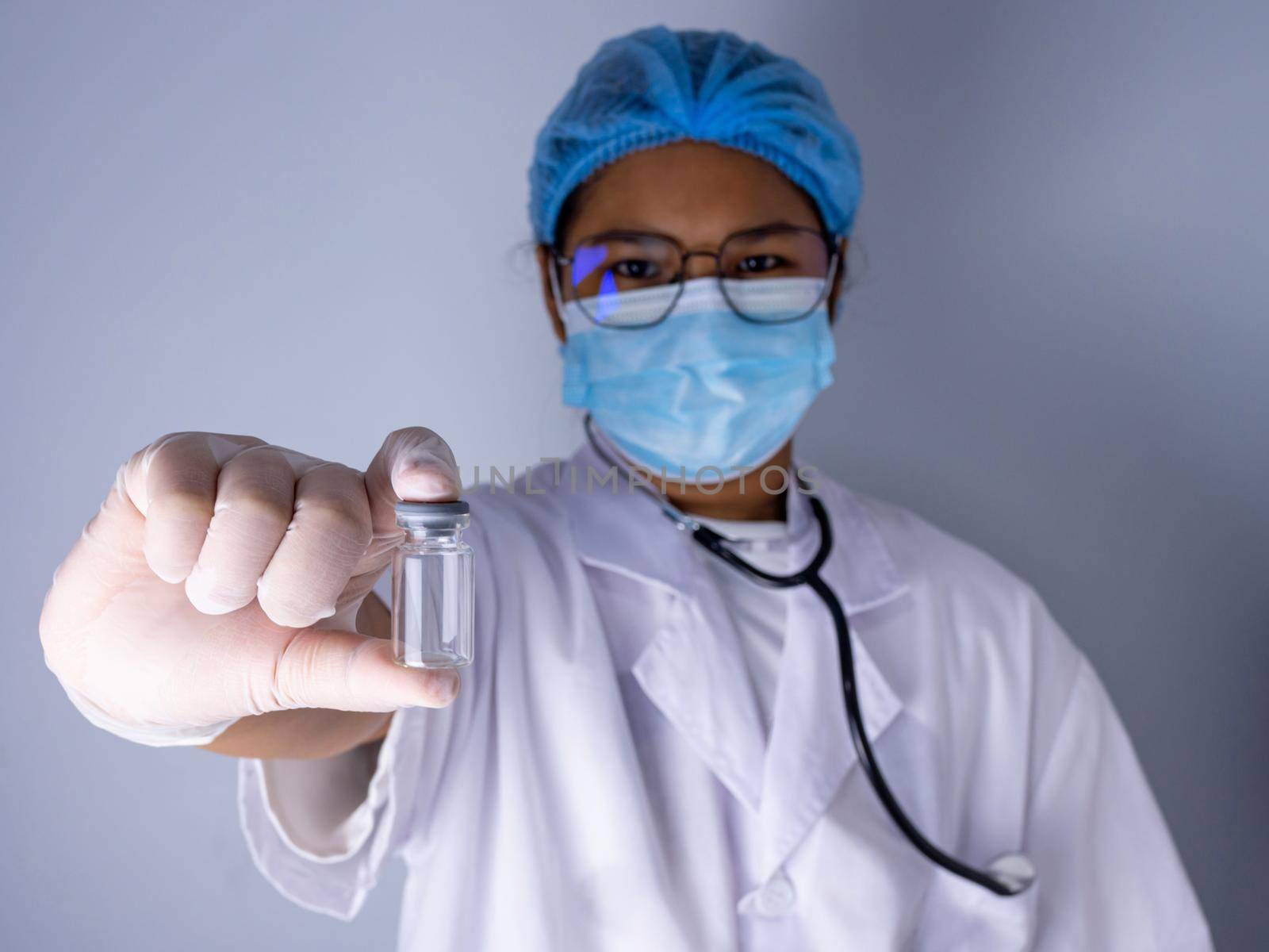 Portrait of a female doctor wearing a mask and wearing a hat Stand holding an empty vaccine or pill bottle.Medical concept and treatment. by Unimages2527