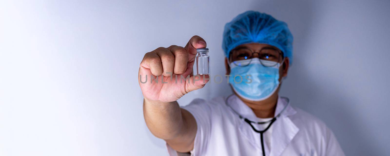 Portrait of a doctor wearing a mask and wearing a hat Stand holding an empty vaccine or pill bottle.Medical concept and treatment. by Unimages2527