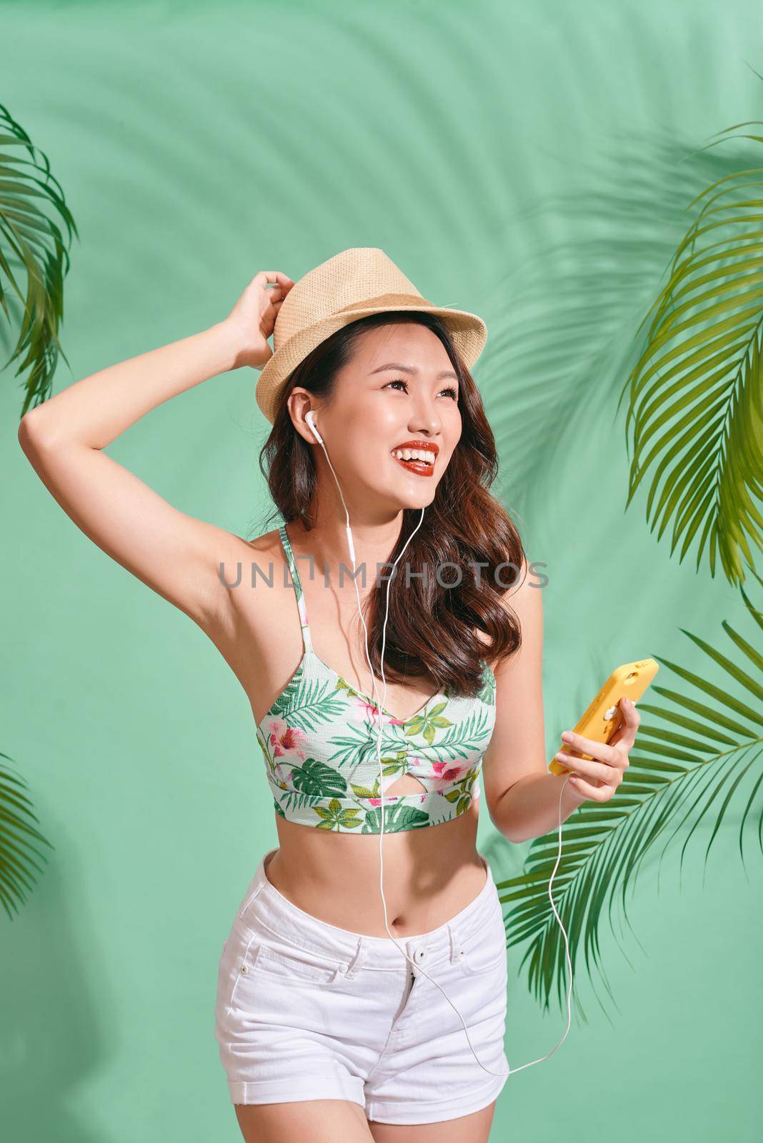 Portrait of happily Asian woman wearing summer clothes and listening to music on the blue background 