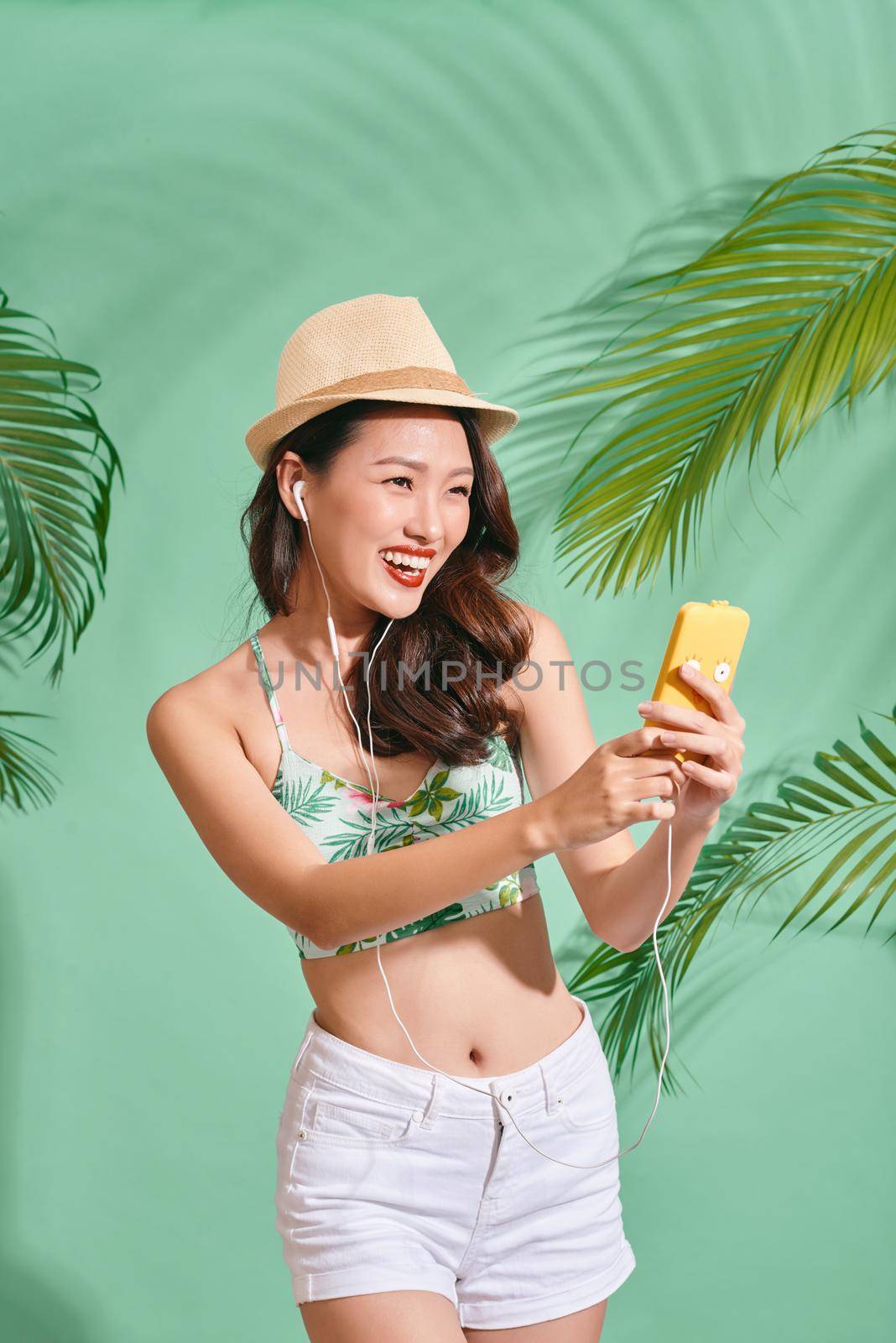 Portrait of happily Asian woman wearing summer clothes and listening to music on the blue background  by makidotvn