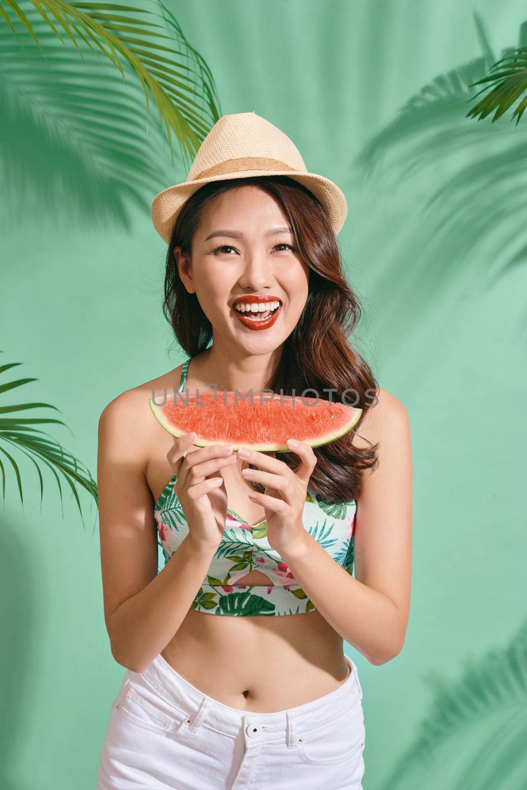 Slice of summer goodness. Beautiful young woman holding slice of watermelon and smiling while standing on blue background