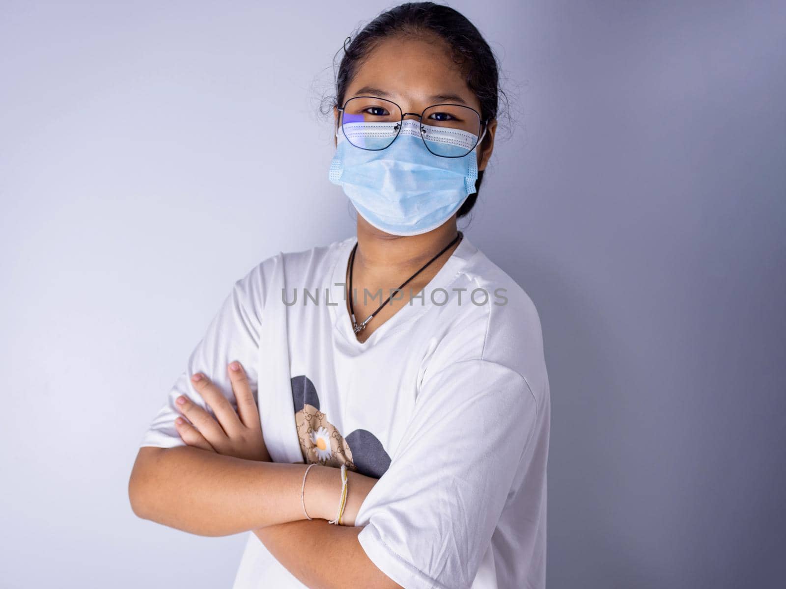 girl wearing a mask and wearing glasses standing with arms crossed on a white background by Unimages2527