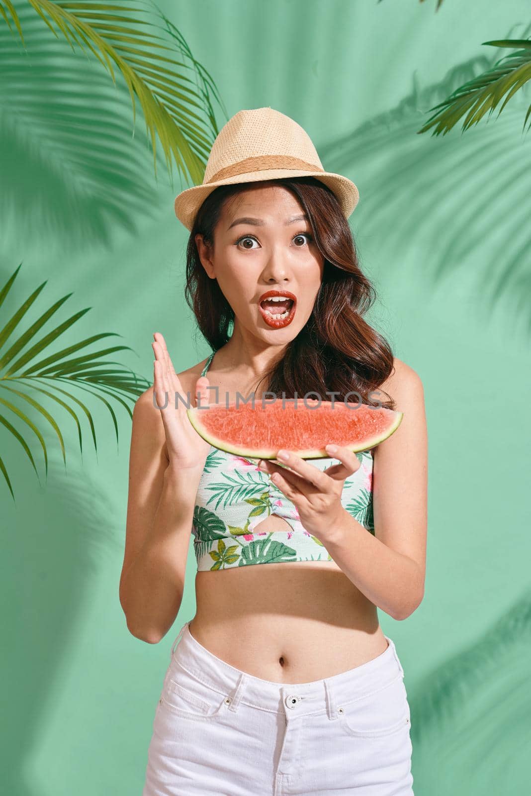 Slice of summer goodness. Beautiful young woman holding slice of watermelon and smiling while standing on blue background by makidotvn