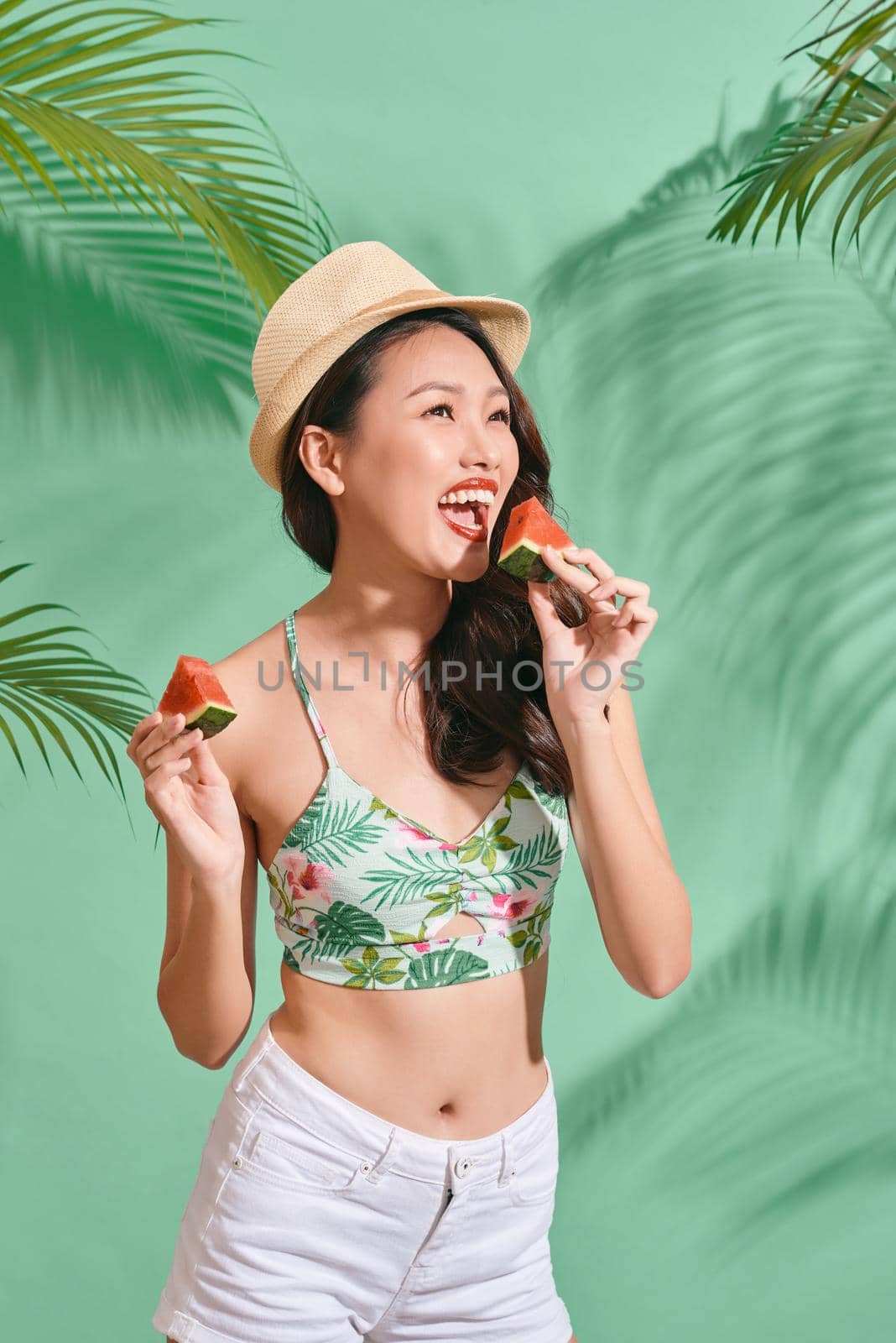 Fashion pretty asian woman is eating a slice of watermelon in the  blue background by makidotvn