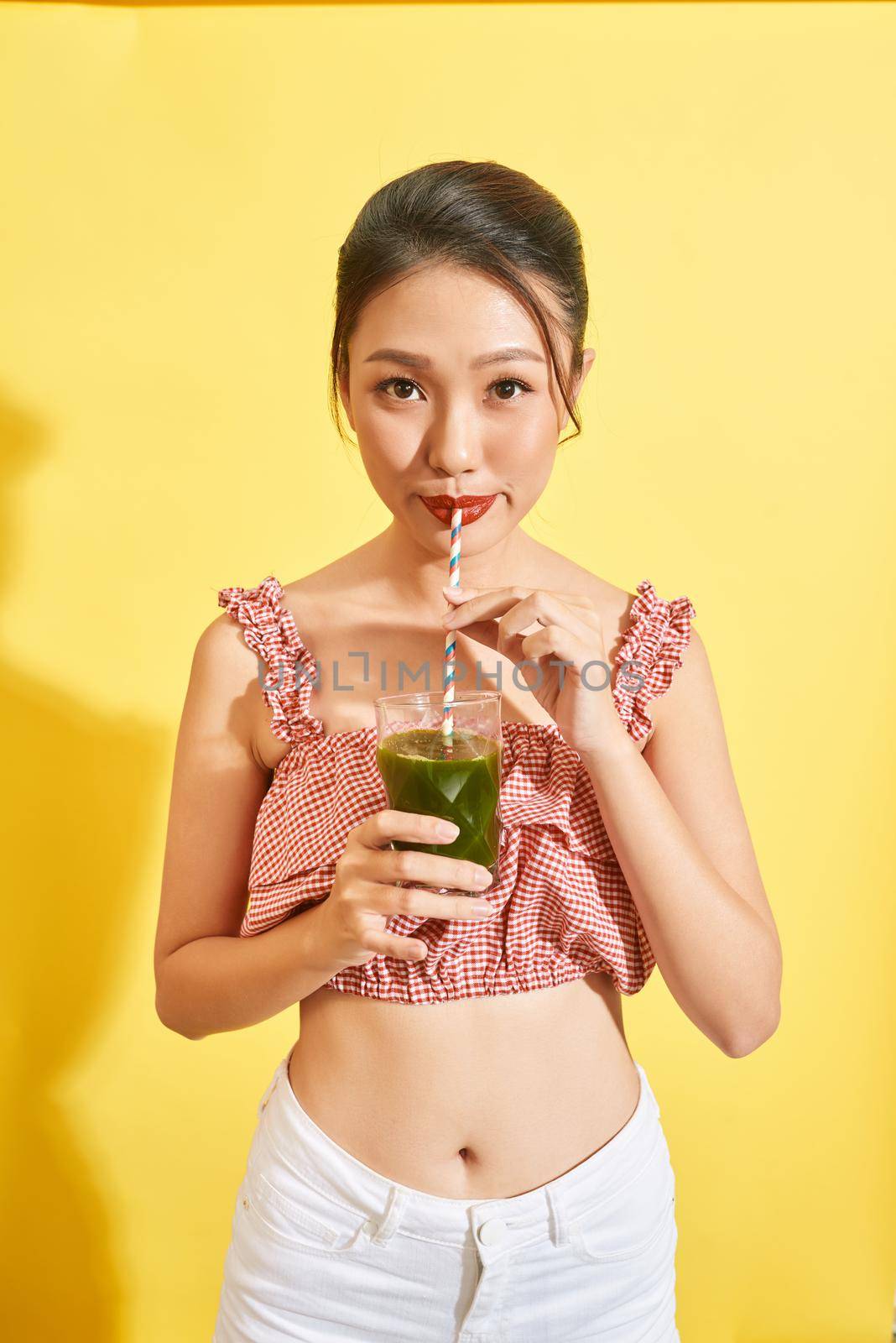 Smiling young asian woman drinking green fresh vegetable juice or smoothie from glass  by makidotvn