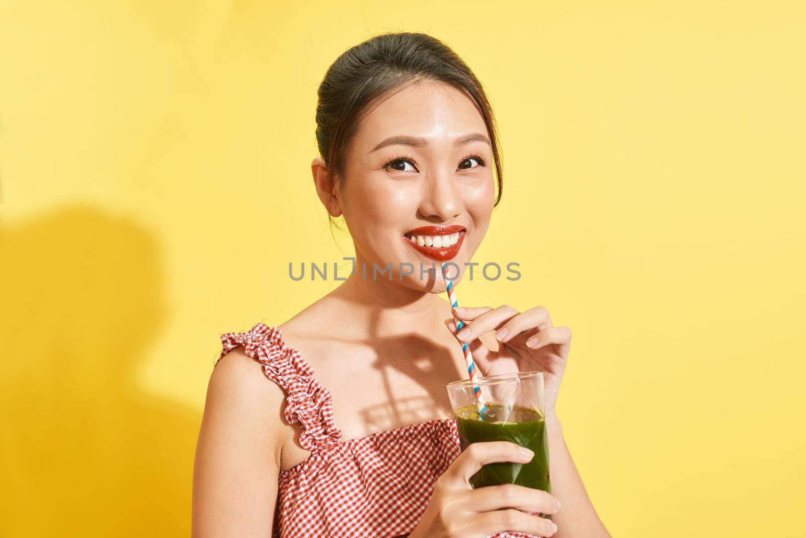 Smiling young asian woman drinking green fresh vegetable juice or smoothie from glass 