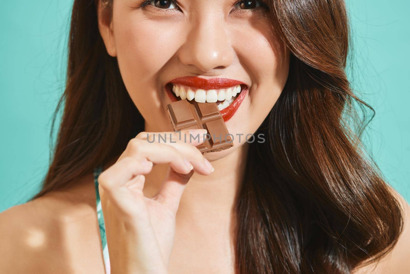 Portrait of a happy young asian woman eating chocolate bar isolated over white background  by makidotvn