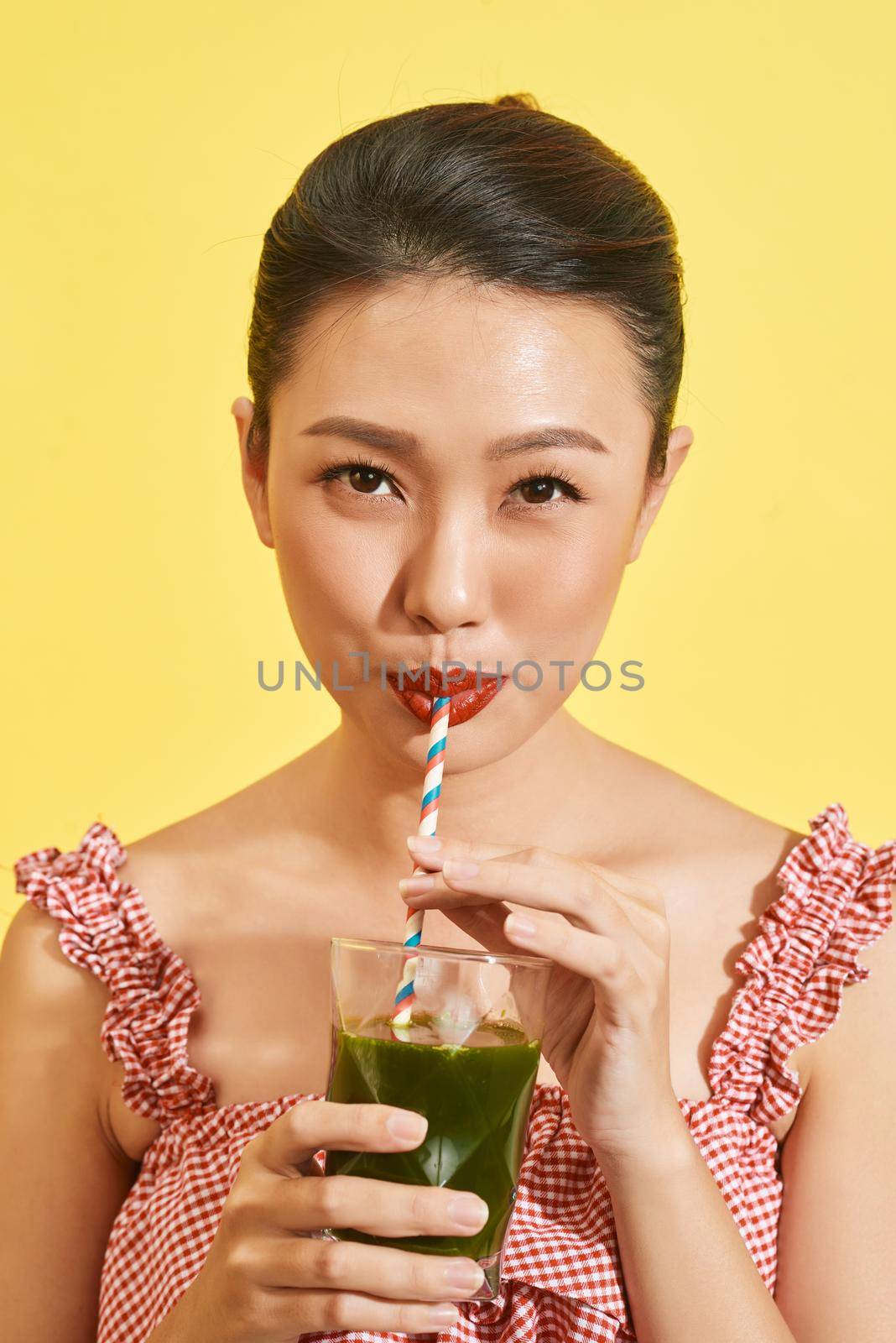 Smiling young asian woman drinking green fresh vegetable juice or smoothie from glass 