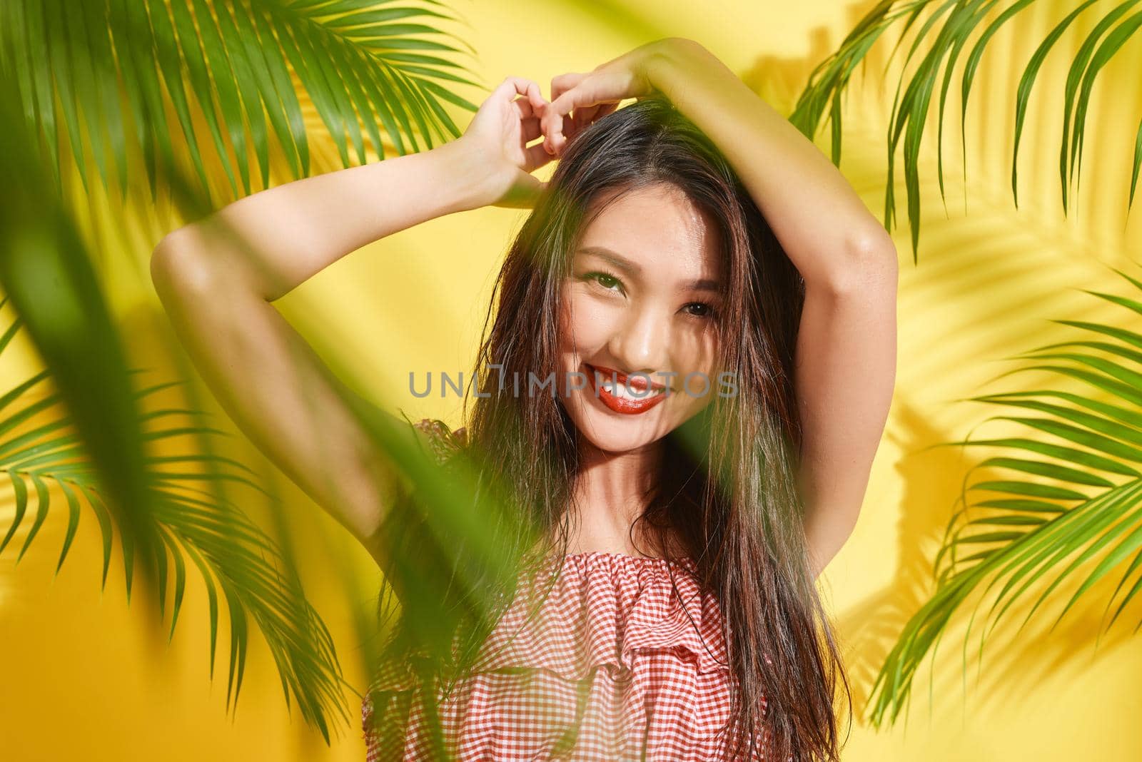A beautiful girl with wet hair stands among palm leaves in yellow background