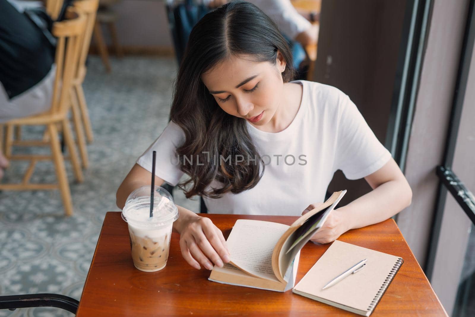 Portrait of Asian woman reading book in coffee shop cafe vintage color tone by makidotvn