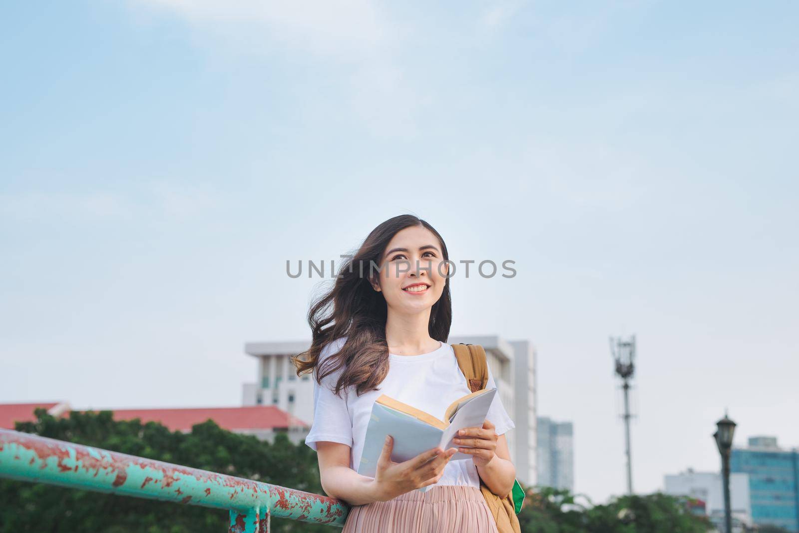 Young beautiful girl reading book  on a bridge with city view