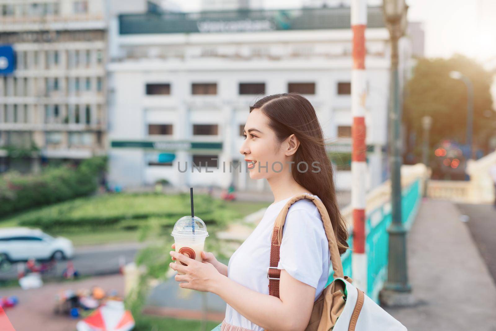 Young beautiful girl standing on a bridge with city view with coffee cup in her hand.