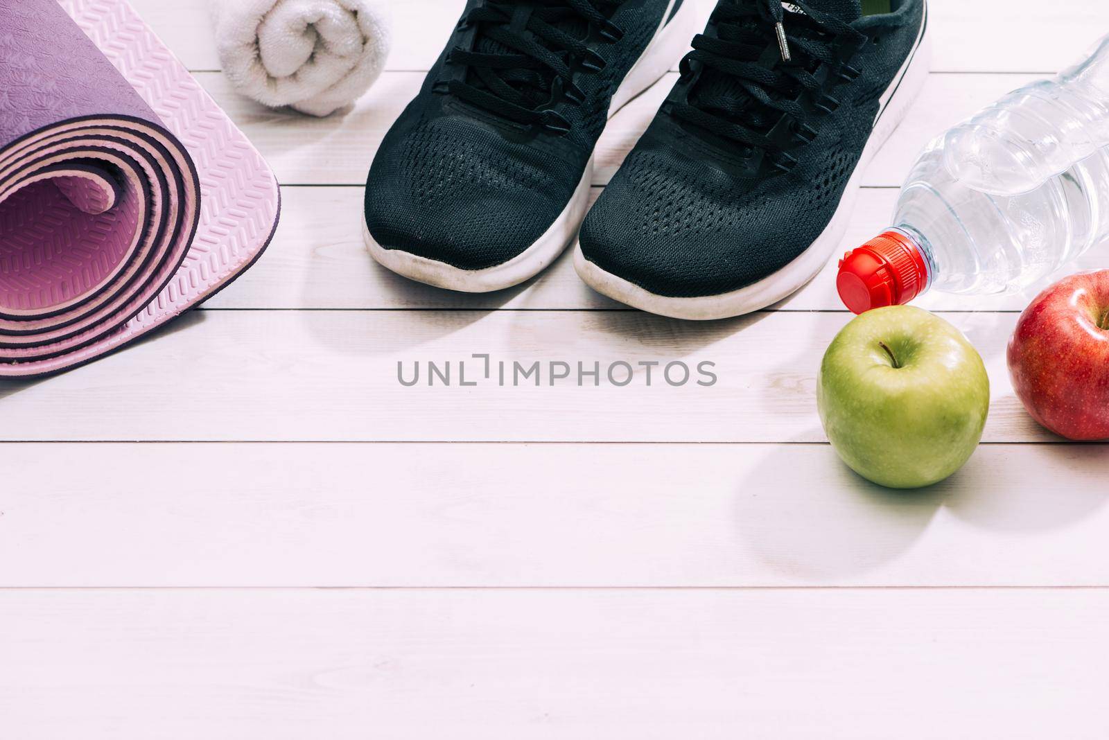 Ladies Sports Accessories such as trainers shoes, dumbbells, yoga mat with water and apple. Fitness, sport and healthy lifestyle concept. Top view, copy space