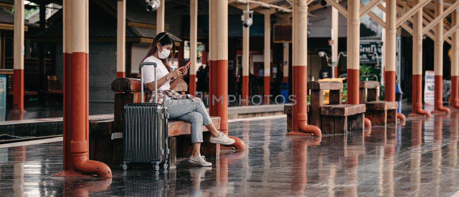 Asian tourist teenage girl at train station using smartphone for online map, social media check-in, or buy ticket booking. Modern travel app technology, lone traveler