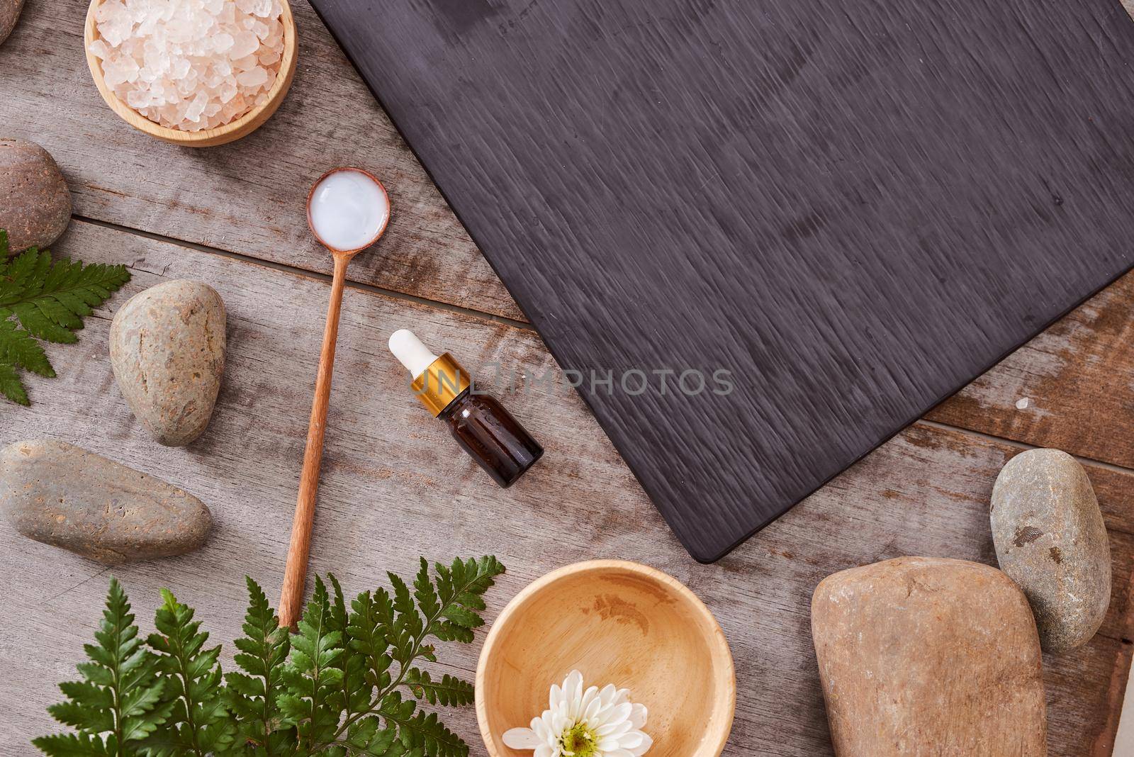 beauty product samples and bath salt with evergreen leaves and black stone on  wood table
