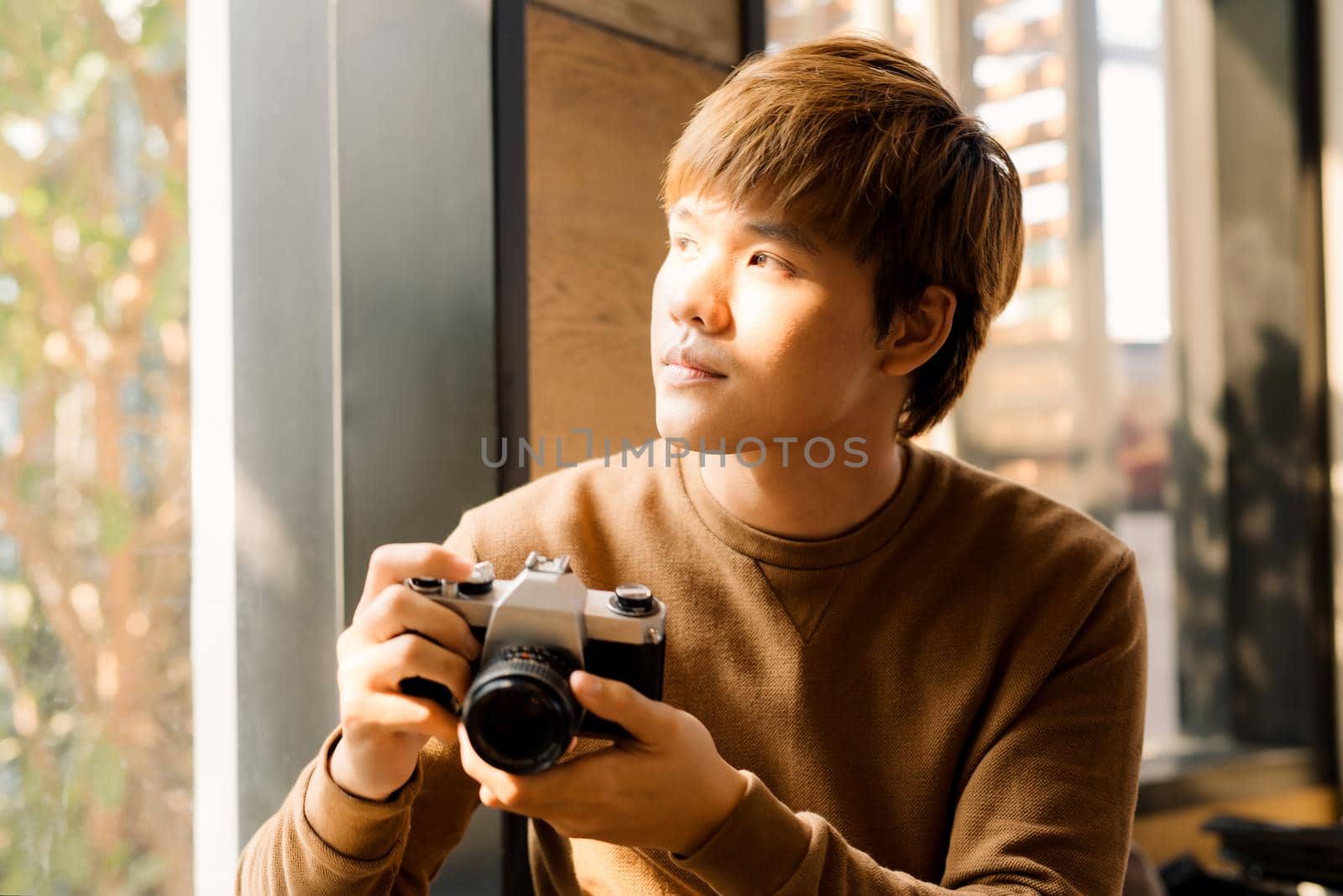 Cropped view of male amateur dressed in yellow sweater making setting on display of vintage camera for cool pictures.Professional photographer checking photos on antique device resting in coffee shop by makidotvn