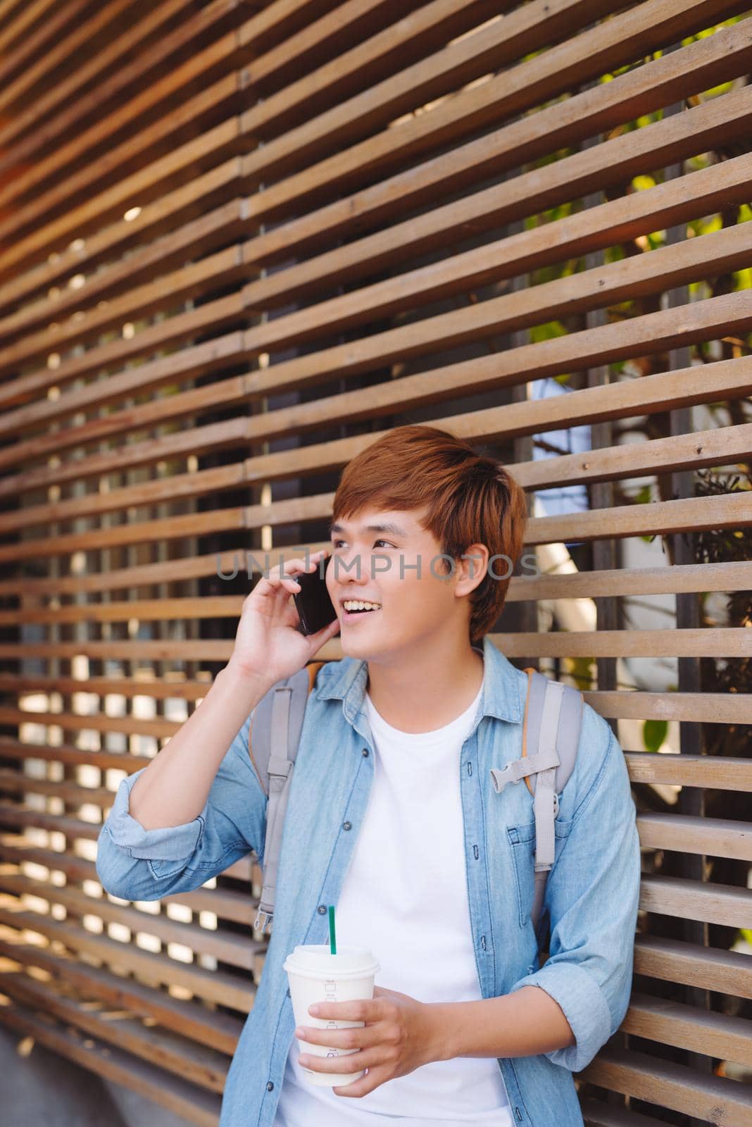 Young asian man smiling and talking on mobile phone outside with copy space on the left