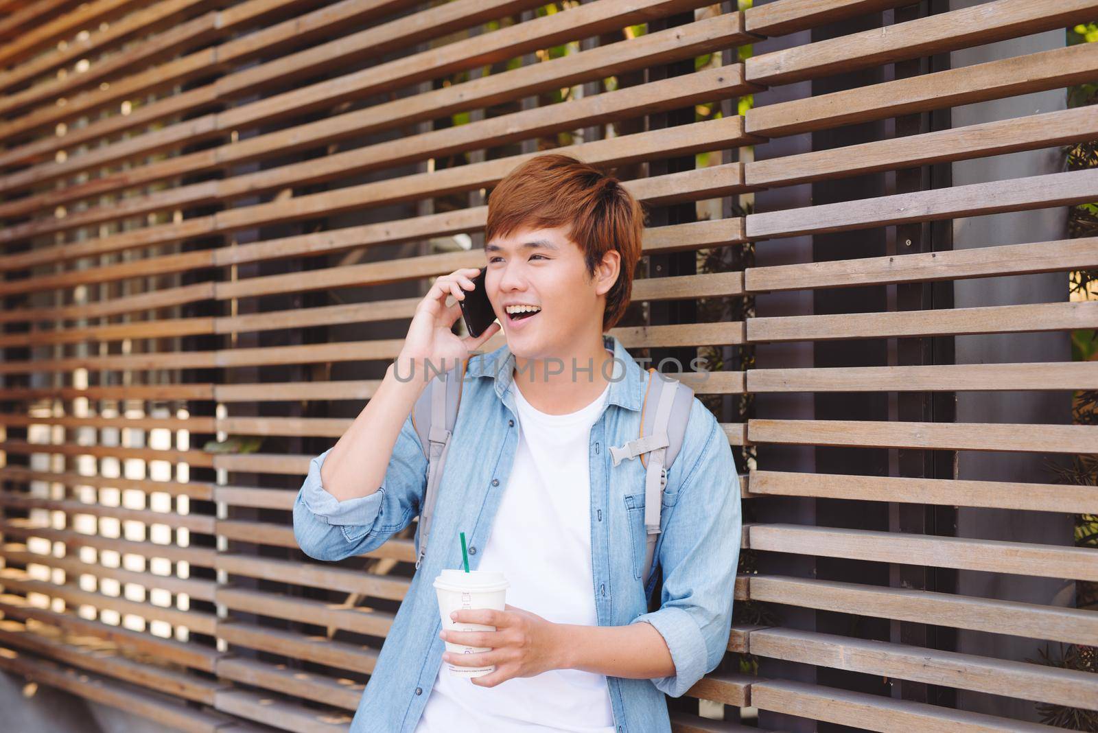 Young asian man smiling and talking on mobile phone outside with copy space on the left by makidotvn
