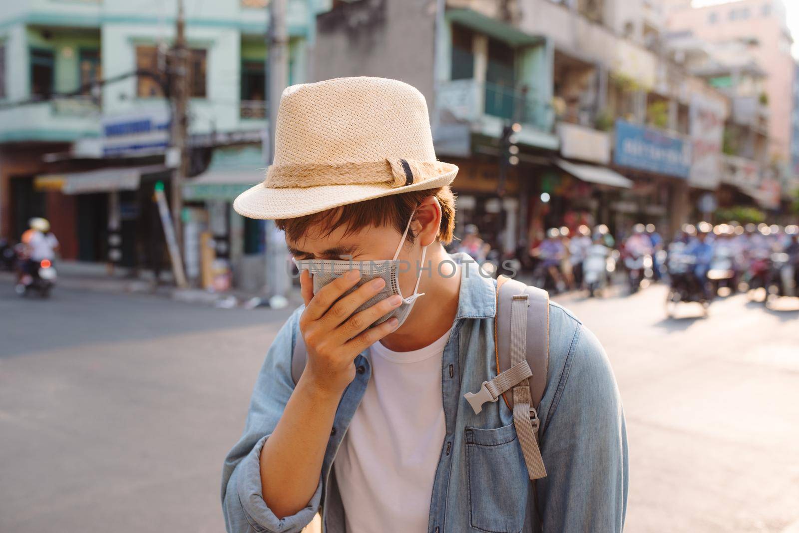 Young man in protective mask feeling bad on the street in the city with air pollution by makidotvn